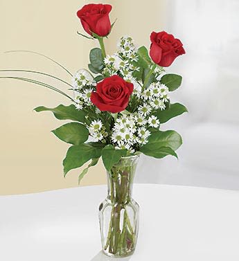 Tall arrangement of three red roses with small white daisies in a clear glass vase