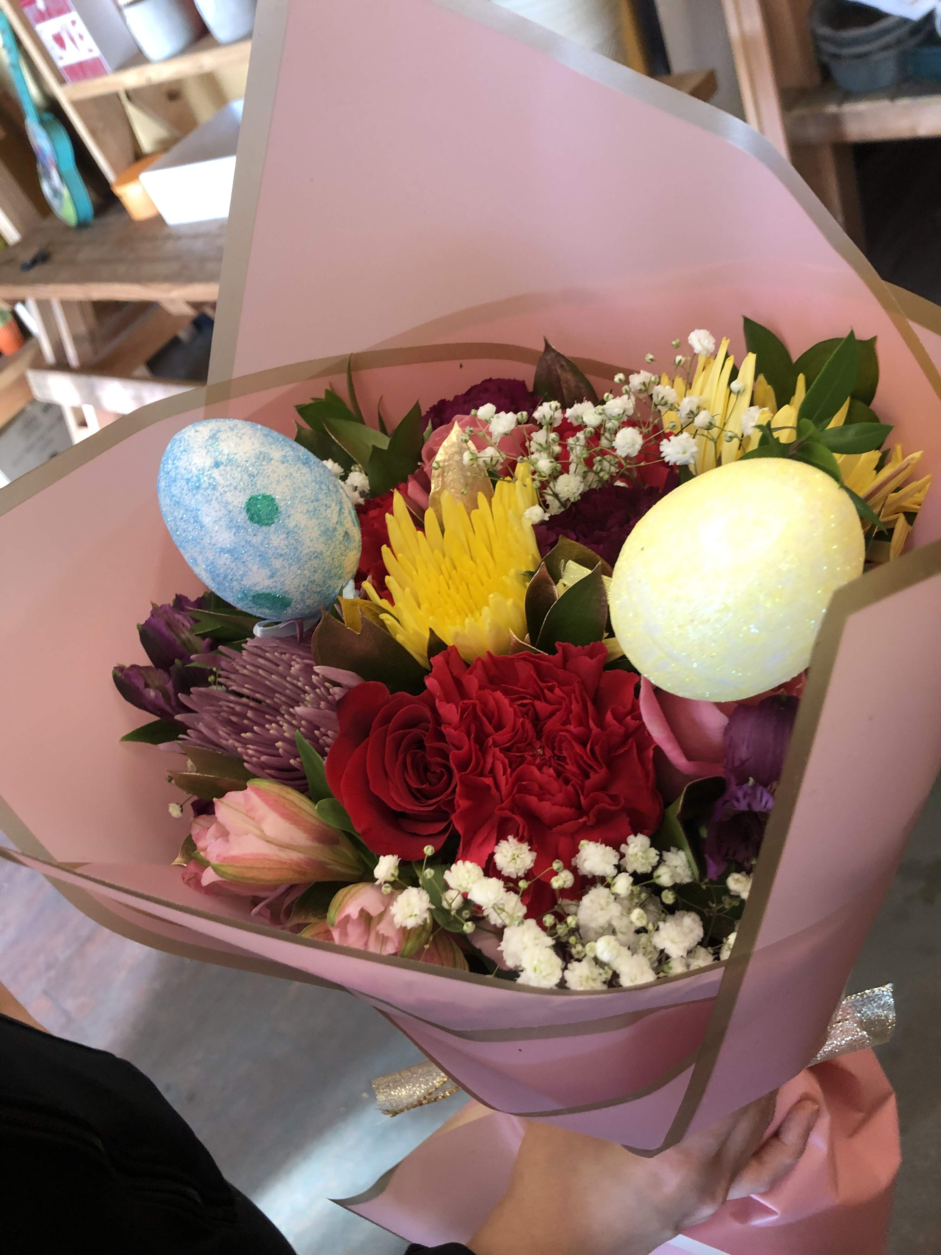 Hand-tied bouquet of bright mixed flowers with decorative pastel eggs wrapped in pink paper