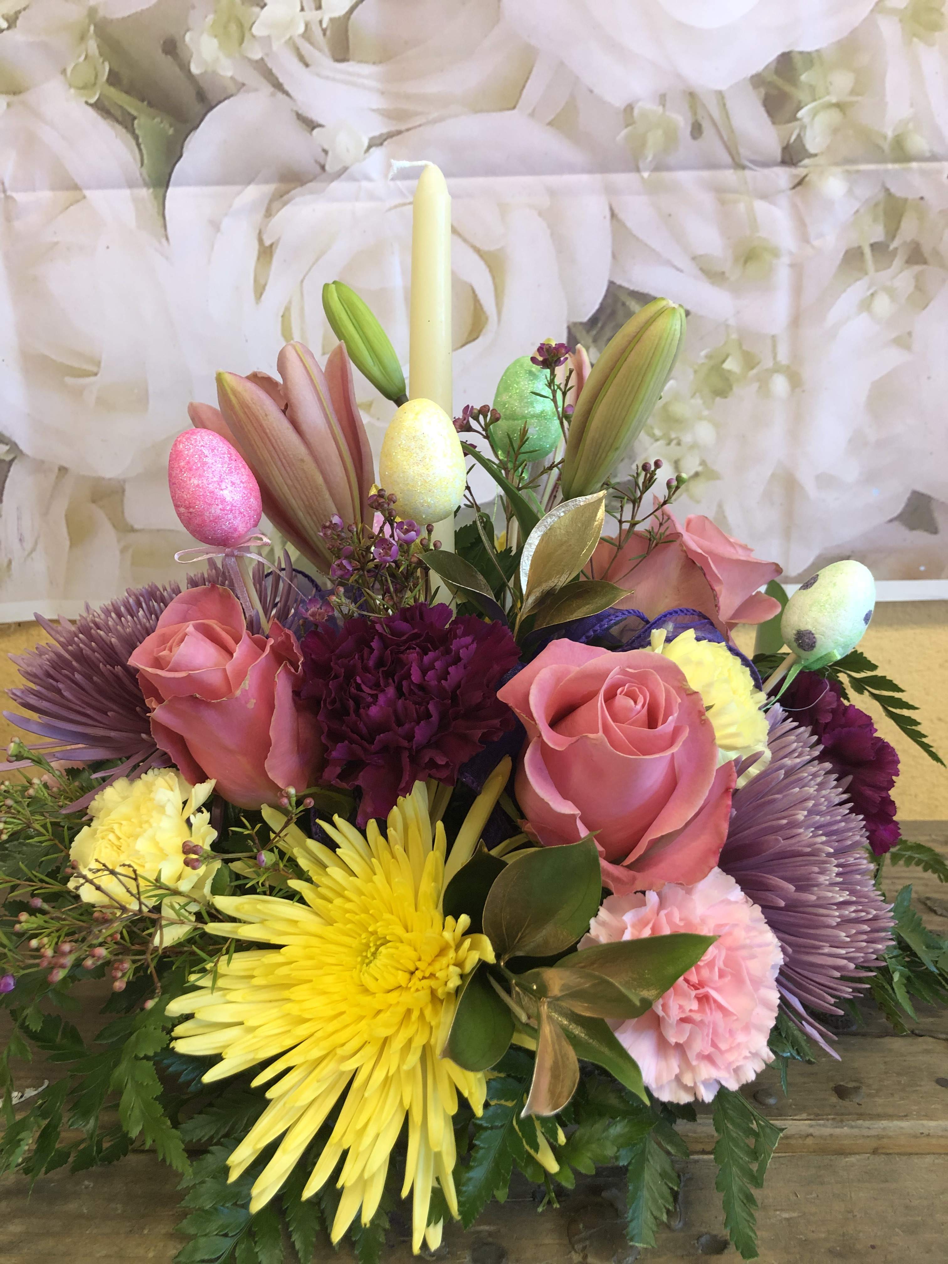 Easter Centerpiece (Designer Choice) - To include a mixture of flowers to include roses, carnations, spiders, lilies and gold ruscus with ia candle and colorful plastic eggs on a stick to give it a unique touch.  We will use pink, purple, yellow flowers. 