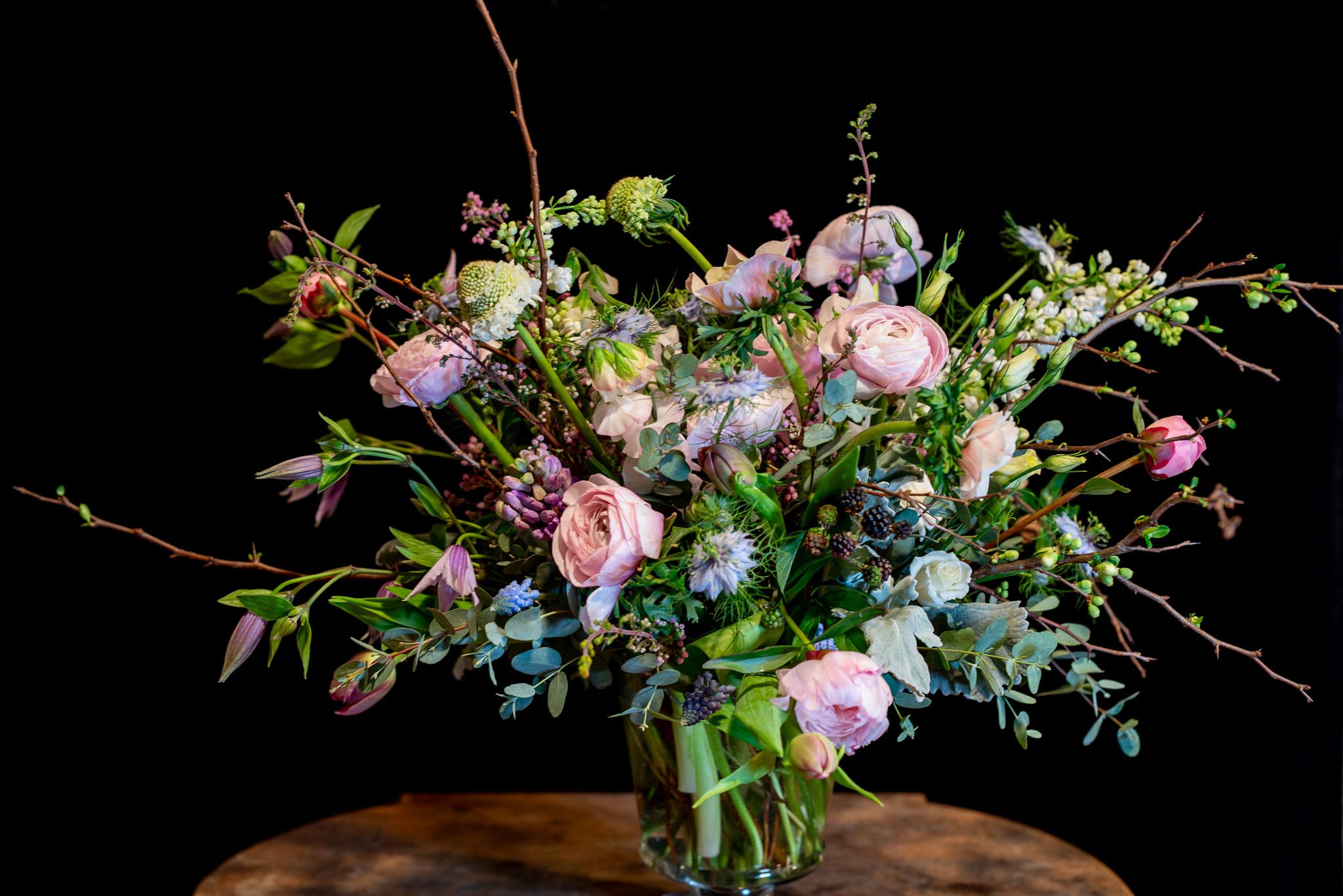 Spring Lavenders and Pinks - A Dutch Masters inspired spring design using flowering branches, premium ranunculus, peonies, and lilac among other beautiful spring garden flowers.  Soft lavender pinks enhance the beauty in this tall centerpiece.  