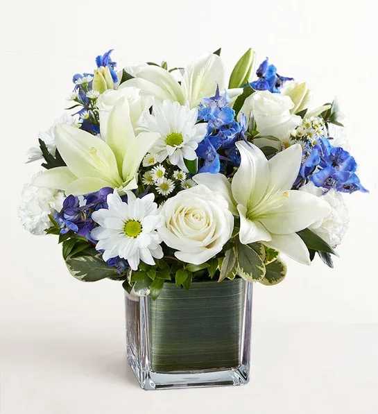 Healing Tears Blue &amp; White - Soothe their tears as they mourn the loss of a loved one with the serenity of blue and white. Our sympathy arrangement of fresh blue delphinium, white roses and lilies, expertly gathered together in a clear glass cube lined with Ti leaf ribbon, makes for an exquisite gesture of comfort and healing.