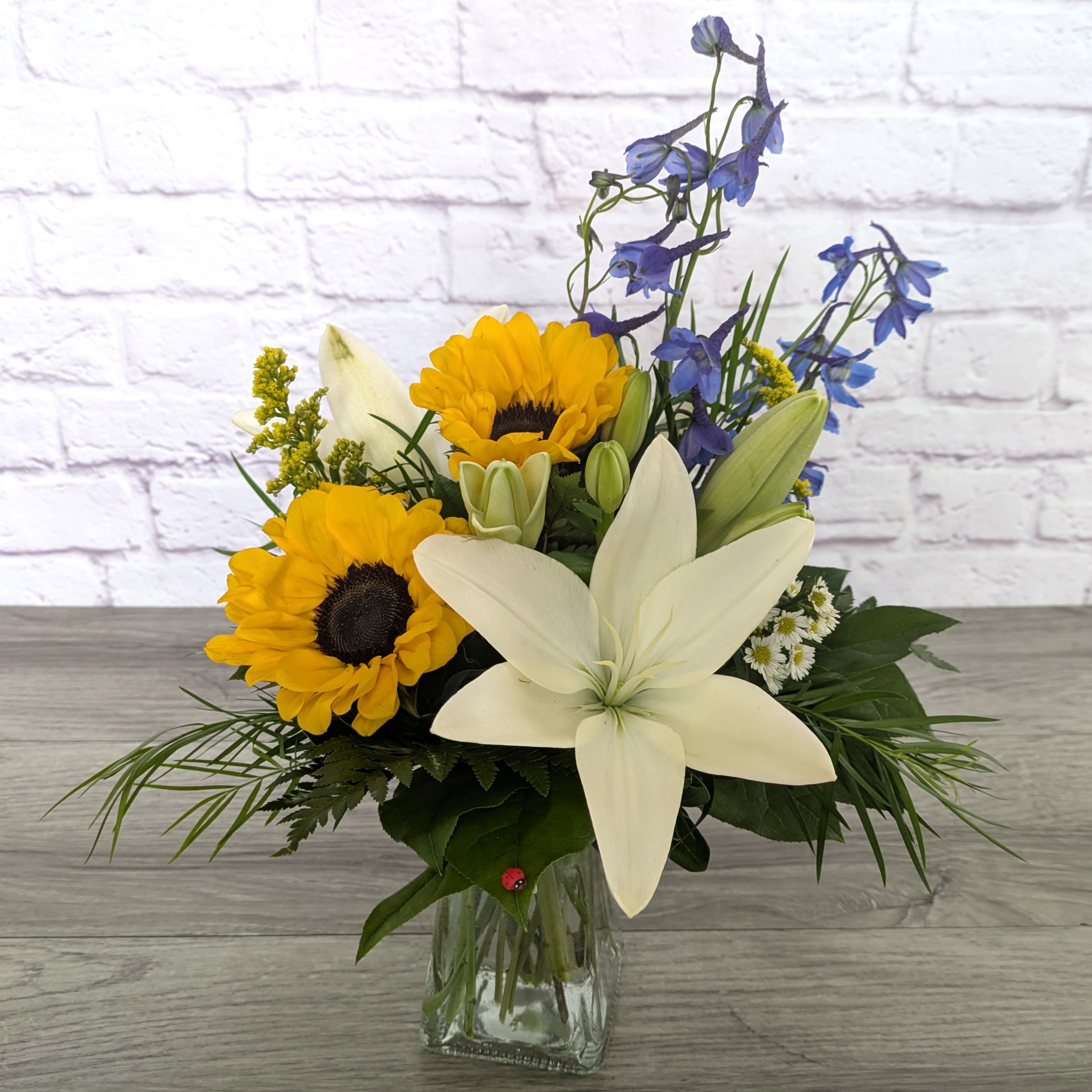 Day’s In The Sun - Day’s In The Sun is A Ladybug Floral exclusive bouquet. This bouquet features sunflowers, lilies, delphinium, solidago and monte casino aster. A visual representation of the bright summery days here in Colorado.   All Around 18”H X 12”W 