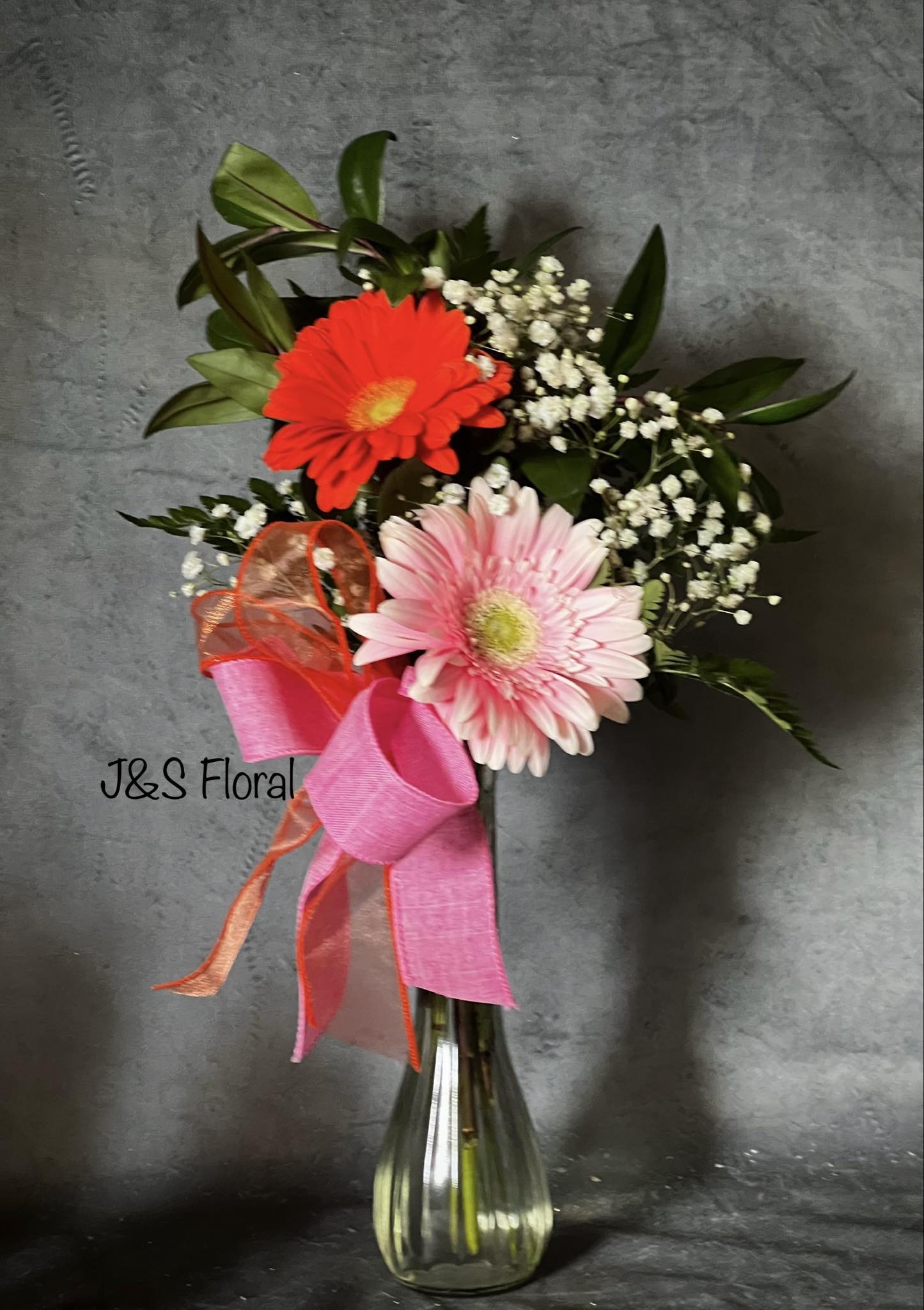 Pink and red gerbera bouquet in a glass vase with ribbon
