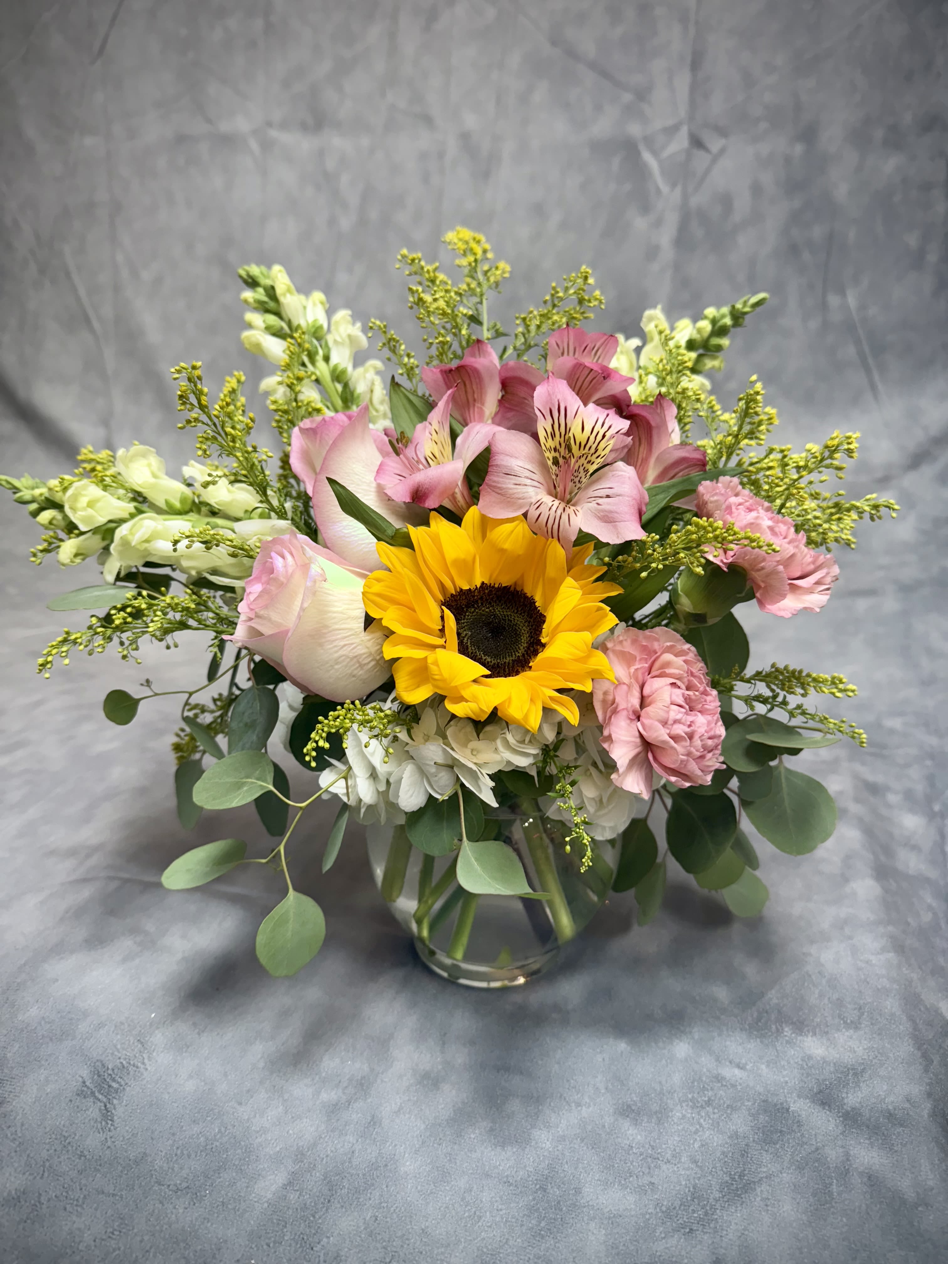 Bouquet of sunflowers, pink alstroemeria, and carnations in a glass vase