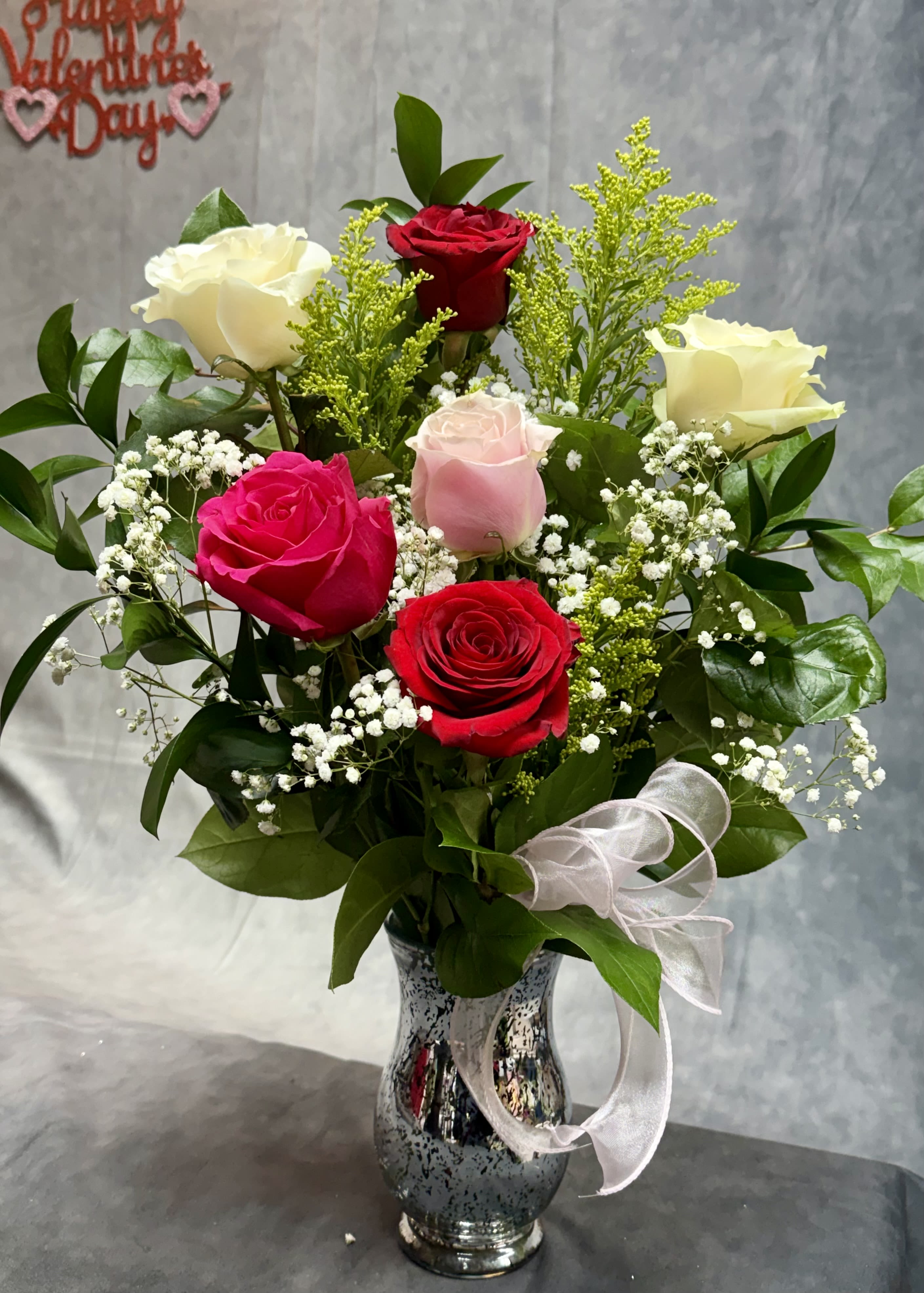 Mix Roses Front Face Vase - A charming mixed-rose arrangement featuring red, pink, and white roses accented with fresh greenery and golden filler, elegantly styled in a vase and finished with a soft pink ribbon—perfect for expressing love, appreciation, or a sweet everyday surprise. 