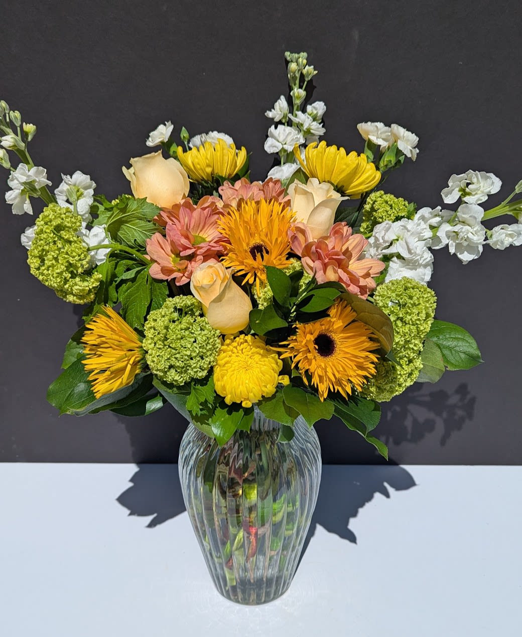 Garden Whisper Arrangement - Embrace the Gentle Beauty of the Garden Whisper Arrangement  The Garden Whisper Arrangement is a fresh, spring-inspired design that captures the quiet elegance of a blooming garden. With soft whites, creamy tones, and delicate touches of yellow and peach, this arrangement features:  -Viburnum -Yellow and peach chrysanthemums -Yellow gerbera daisies -White mini carnations -White stock -Cream roses  Immerse yourself in the airy charm of the Garden Whisper Arrangement, perfect for brightening any space with a sense of calm, warmth, and effortless spring beauty.