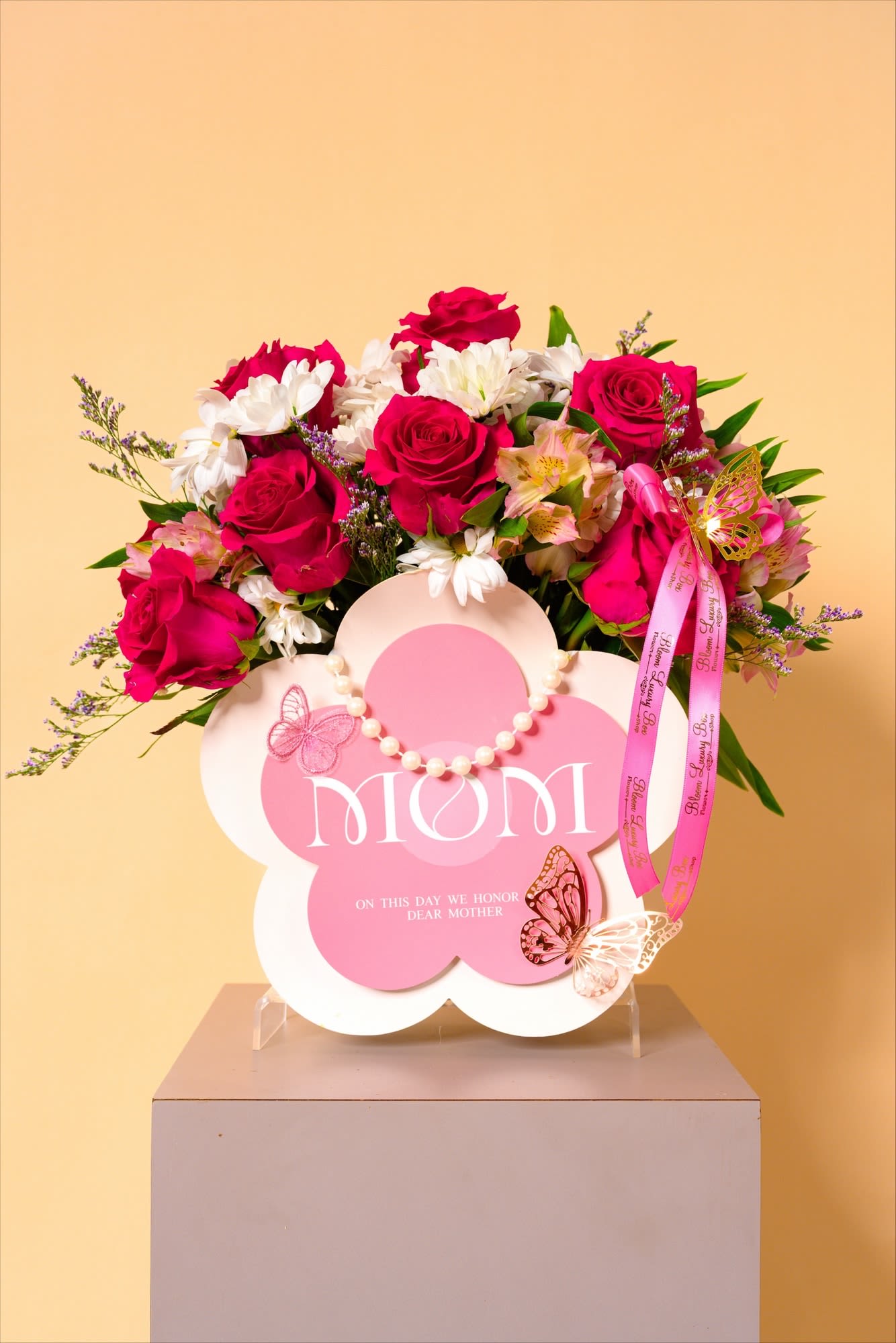 Blush of Gratitude - A radiant arrangement of vibrant pink roses and soft white blooms, this piece captures the warmth and tenderness of heartfelt appreciation. Accented with delicate butterflies and a graceful pearl touch, it feels both elegant and lovingly personal. Perfect for celebrating a cherished mother or someone who means just as much.