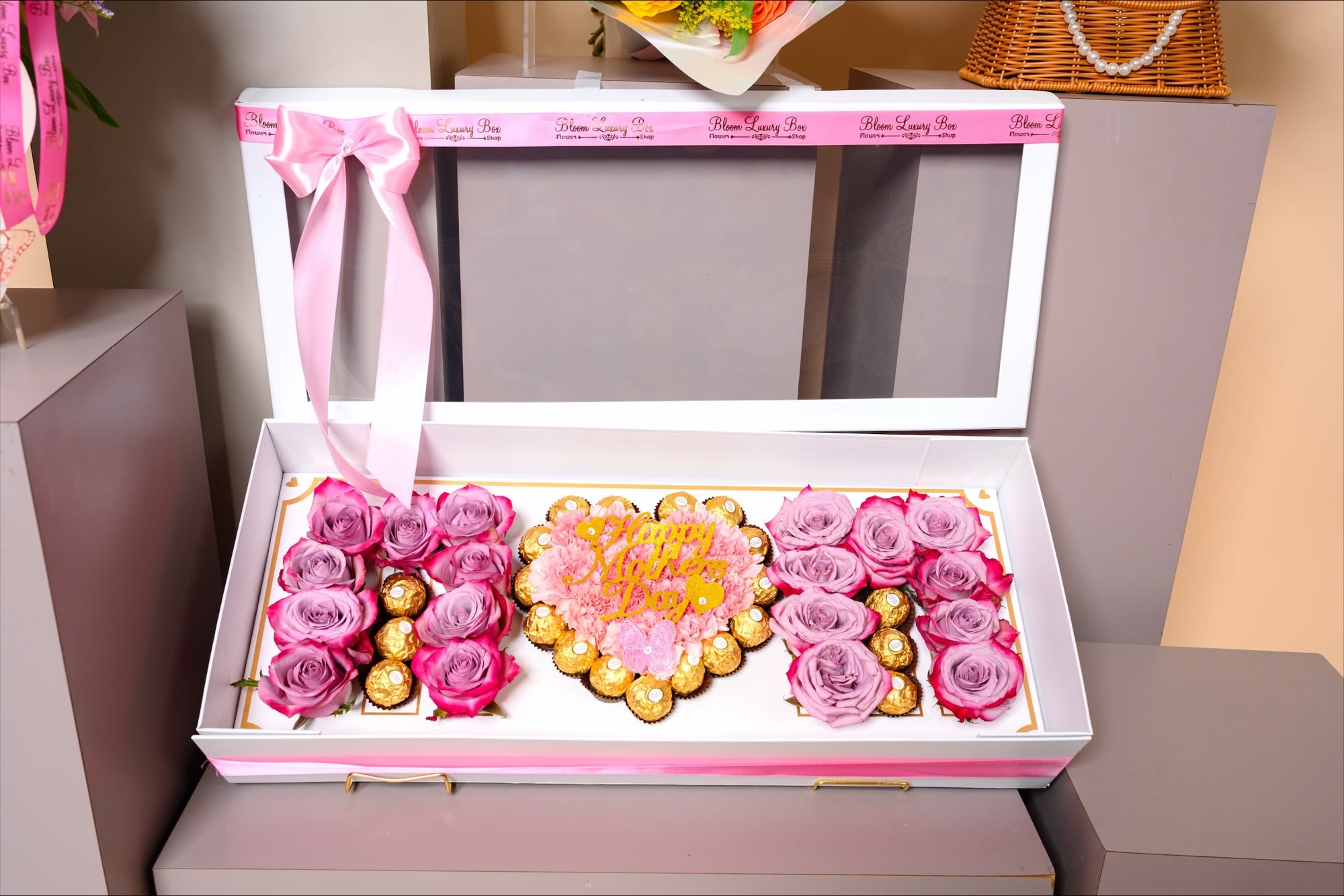Blush Luxe Mother’s Day Gift Box - An elegant keepsake box featuring delicate lavender and pink roses paired with premium chocolate treats, beautifully arranged to spell out a heartfelt message. At its center, a charming “Happy Mother’s Day” design adds a personal and celebratory touch. Finished with a soft pink ribbon, this luxurious gift is the perfect blend of sweetness and sophistication.