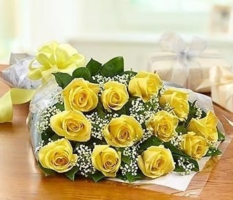 Wrapped bouquet of yellow roses with white filler flowers and a yellow ribbon bow