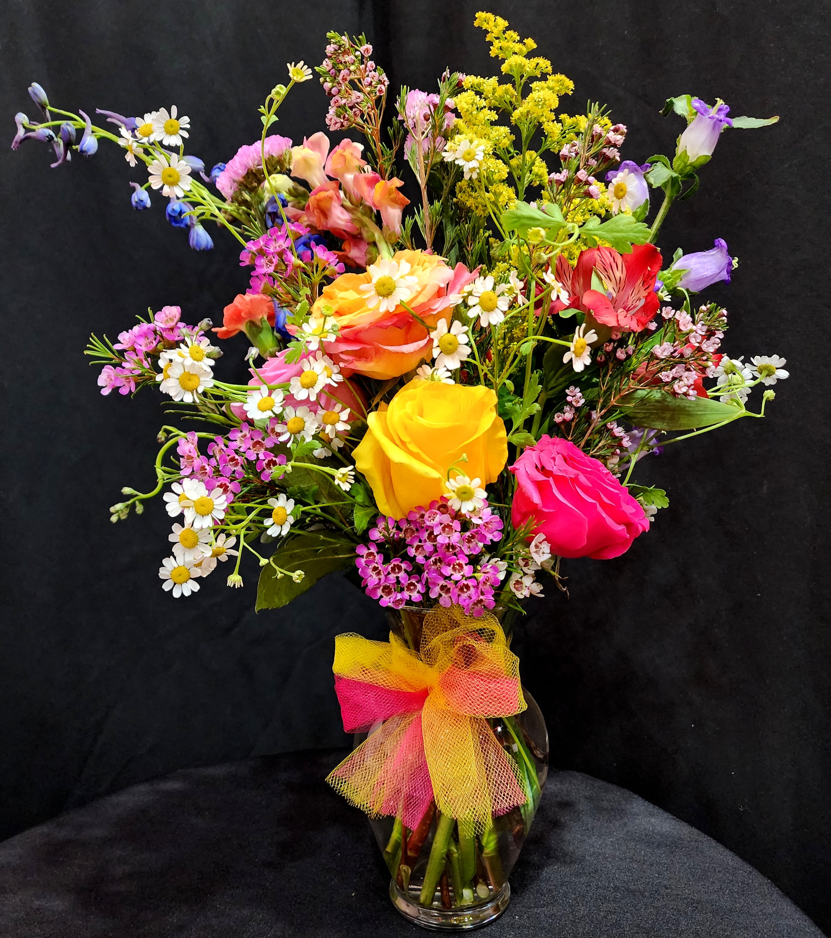 Mini Tucson Sunset - Mini version of our best seller A Tucson Sunset, perfect for the office and small areas such as apartments and studios etc... This beautiful small arrangement includes four different colors of roses, campanulas, delphiniums, snapdragons, wax, chamomile, alstroemeria, eucalyptus and statice.  Comes in a 7" Glass Vase and dimensions are 18" Height x 12" Width x 8" Length. 
