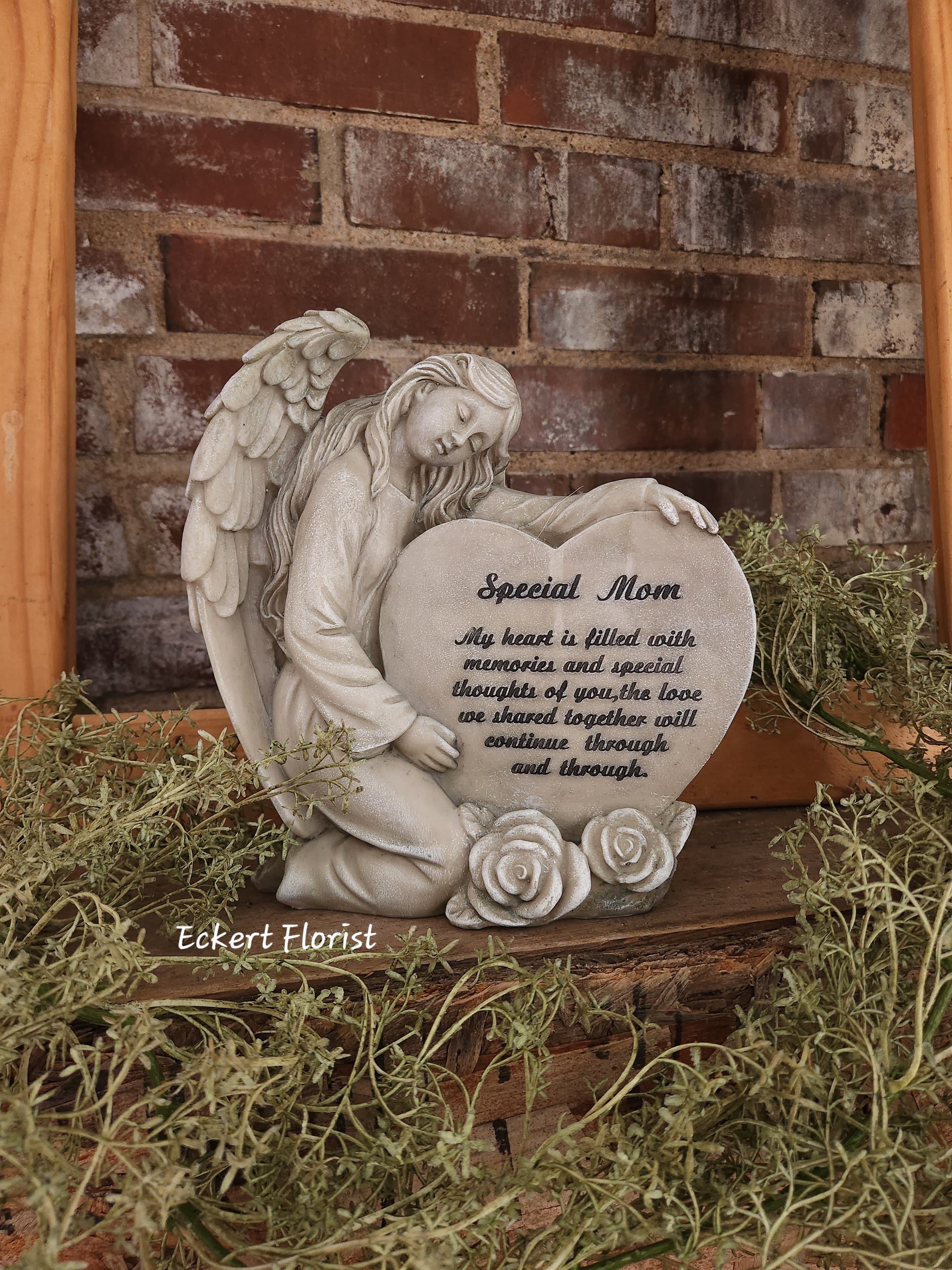 Angel figurine holding a heart-shaped memorial plaque with roses