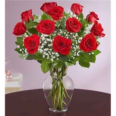 Arrangement of red roses with white filler flowers in a clear glass vase on a dark table