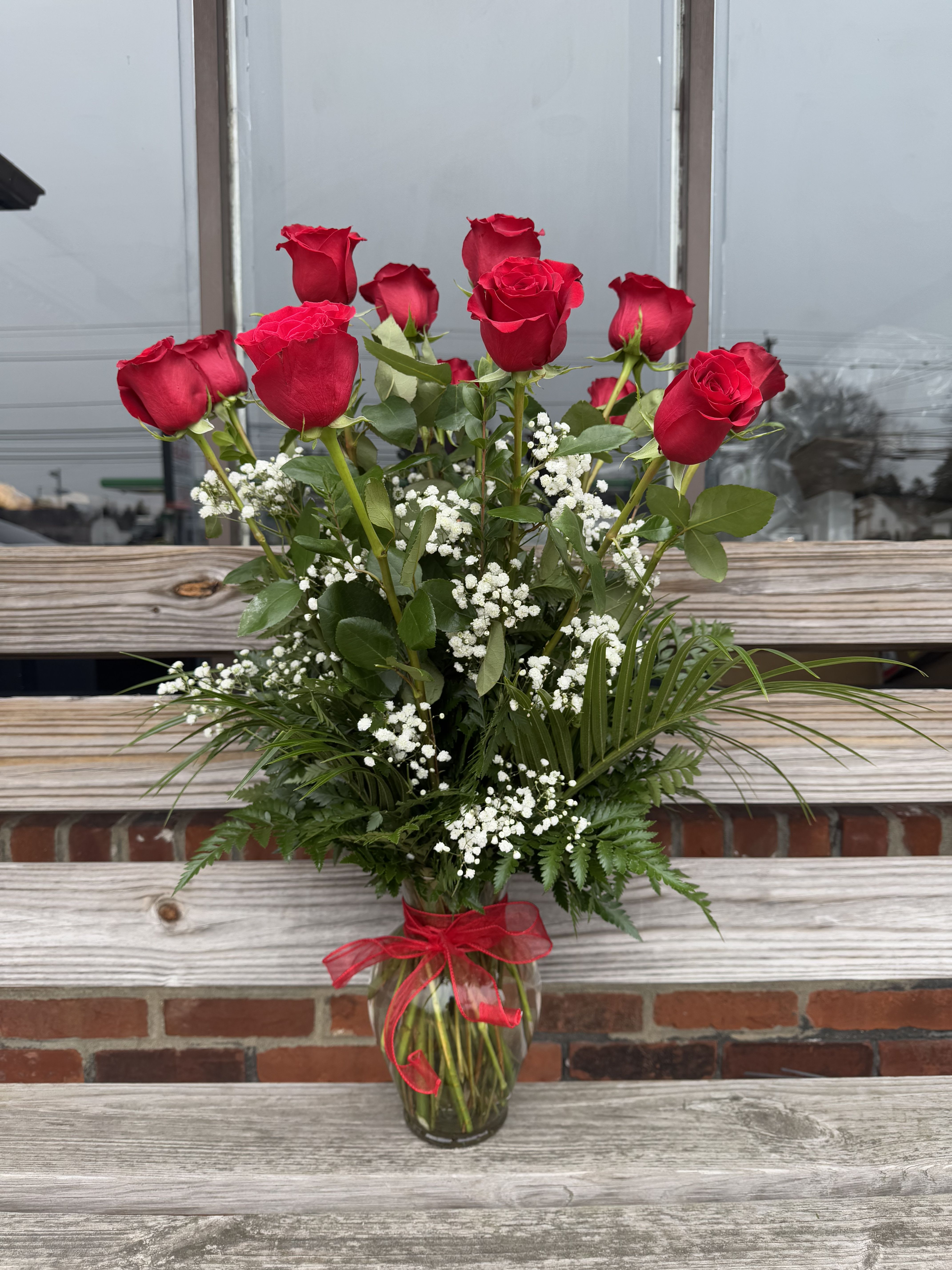 Tall arrangement of red roses with white filler flowers in a clear glass vase with red bow