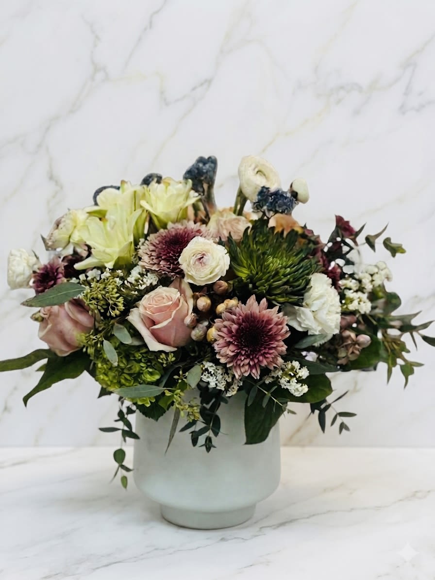 Muted pink and cream flower arrangement with roses, mums, and lilies in a white ceramic vase