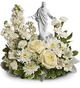 White floral arrangement with roses, carnations, and a central white robed figurine.