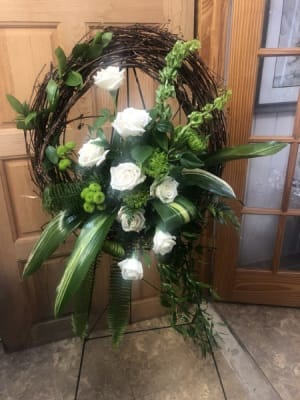 Standing grapevine wreath with white roses and green floral accents on a metal easel