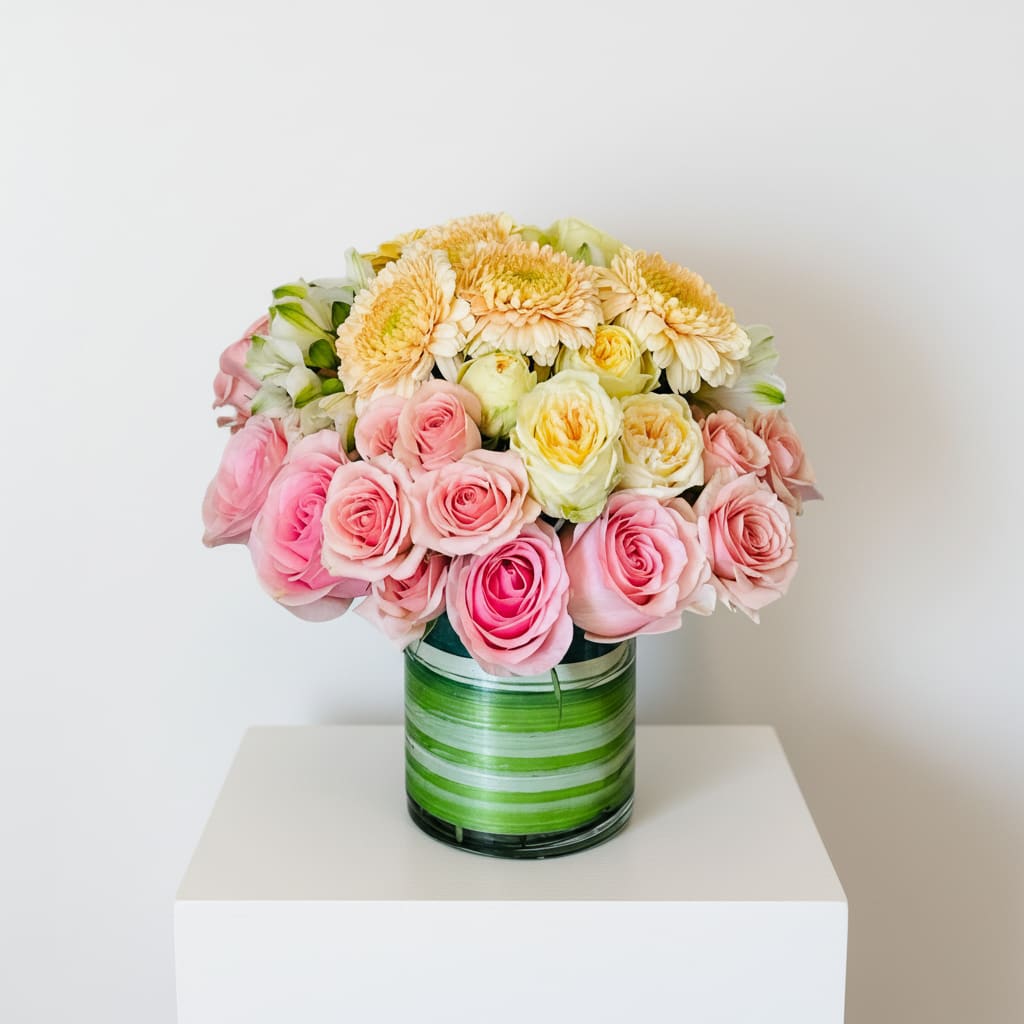 La Créme Arrangement ( Pink, Yellow Garden Roses and Peach Gerbera Daisies) - Soft, elegant, and irresistibly sweet—La Crème is a graceful floral arrangement of blush roses, buttery yellow garden roses, and pale peach Gerbera daisies. Artfully arranged in a clear vase wrapped with striped  green leaves, it’s the perfect gift for birthdays, anniversaries, or simply to brighten someone’s day with creamy pastel charm. 