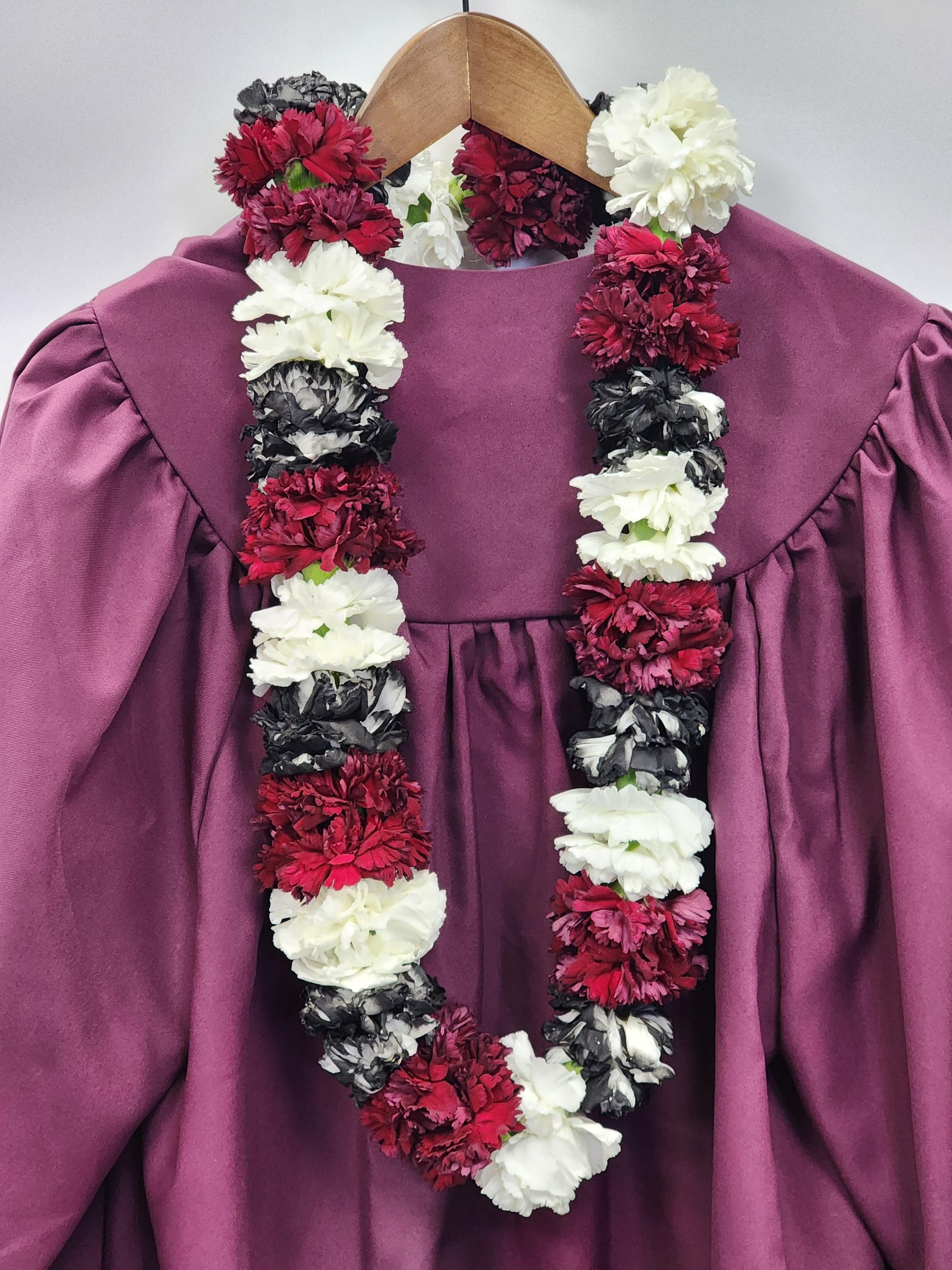 Red, white, and black carnation lei draped over a mauve graduation gown on a wooden hanger
