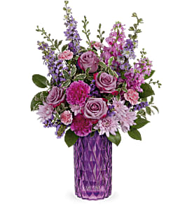 Purple and pink mixed flower arrangement with roses and carnations in a tall purple glass vase