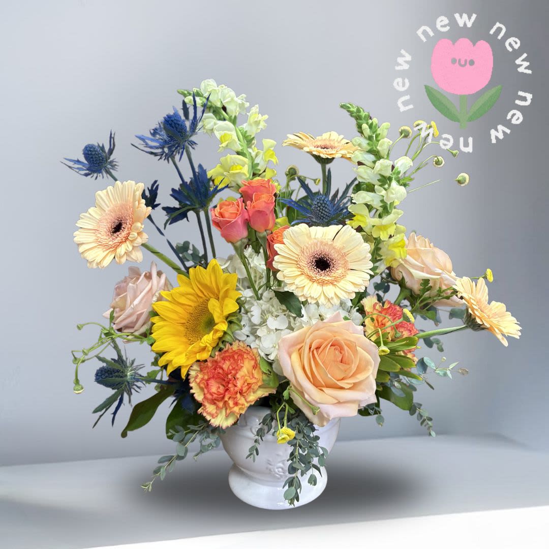 Soft Horizons - A radiant blend of warmth and softness, Sun &amp; Sky captures the feeling of golden light meeting a clear horizon. Featuring buttery yellow sunflowers, soft peach gerbera daisies and roses, and warm-toned carnations, this design is gently accented with touches of cool blue for balance and depth. Joyful yet refined, it’s the perfect arrangement for birthdays, celebrations, or a heartfelt pick-me-up.
