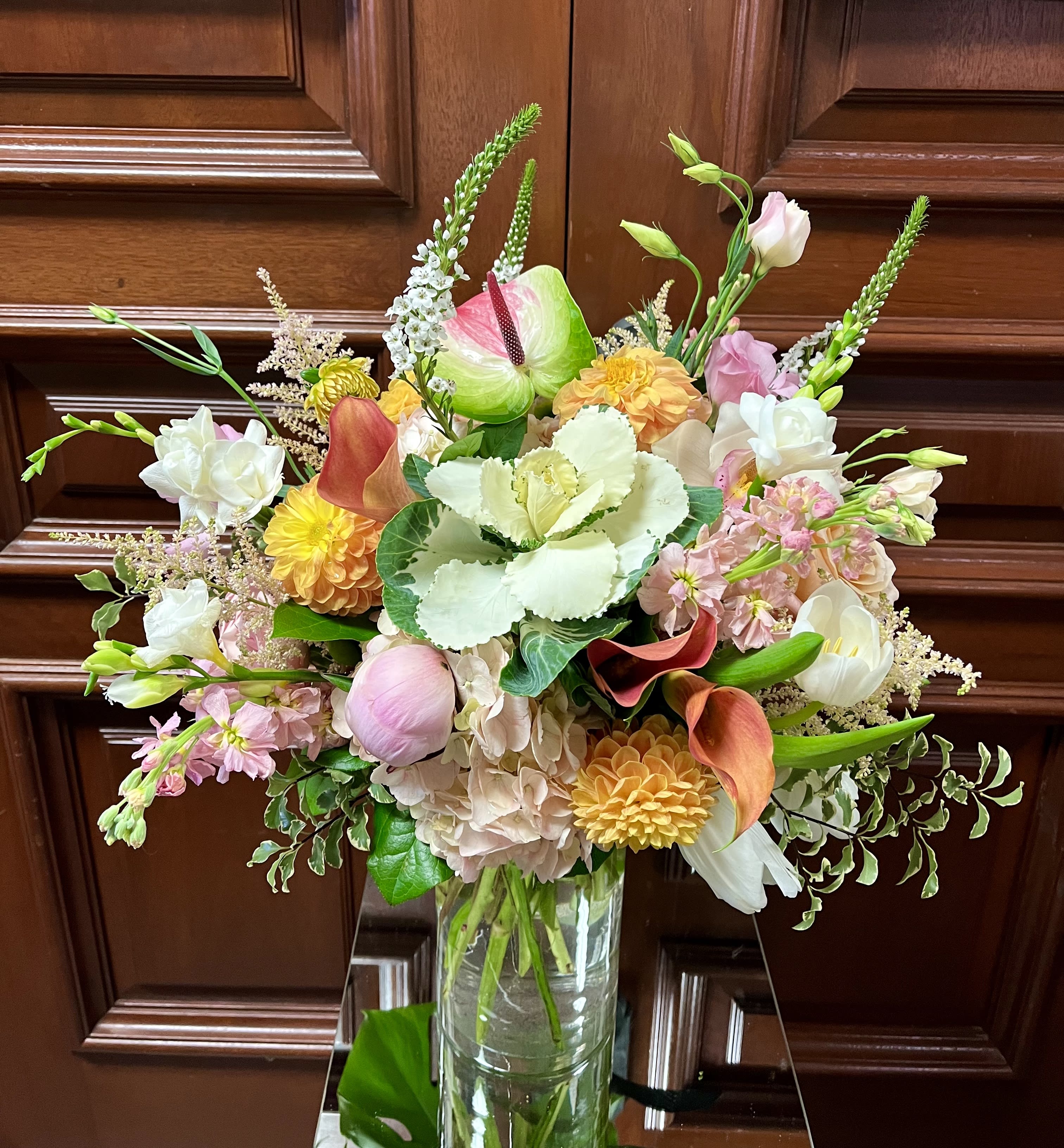 Tall mixed bouquet of pink, peach, yellow, and white flowers in a clear glass vase.