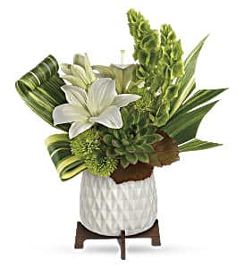 Compact white and green arrangement with lilies, succulents, and tall blooms in a white pot on a wooden stand