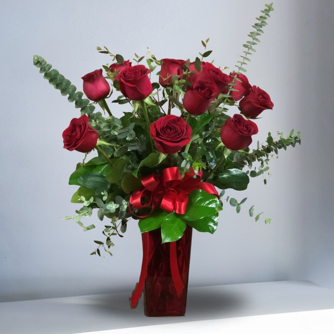 Tall arrangement of red roses in a red glass vase with a red ribbon bow