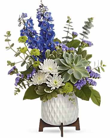 Tall blue delphinium, white mums, purple accents, and a succulent in a white ceramic pot on a wooden stand.