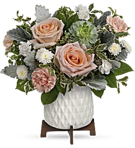 Compact arrangement of peach roses, carnations, and white mums in a white ceramic pot on a wooden stand.