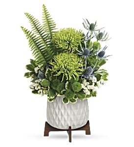 Modern green and blue floral arrangement with spider mums, fern fronds, and thistle in a white pot on wooden stand