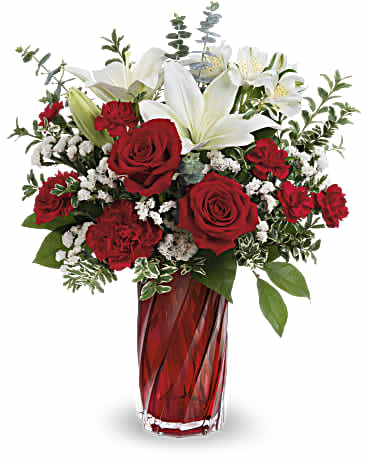 Tall red and white arrangement with roses, carnations, and lilies in a red glass vase