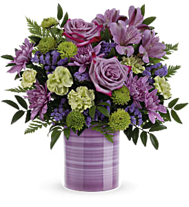 Mixed bouquet of purple roses and blooms with green accents in a lavender striped cylinder vase