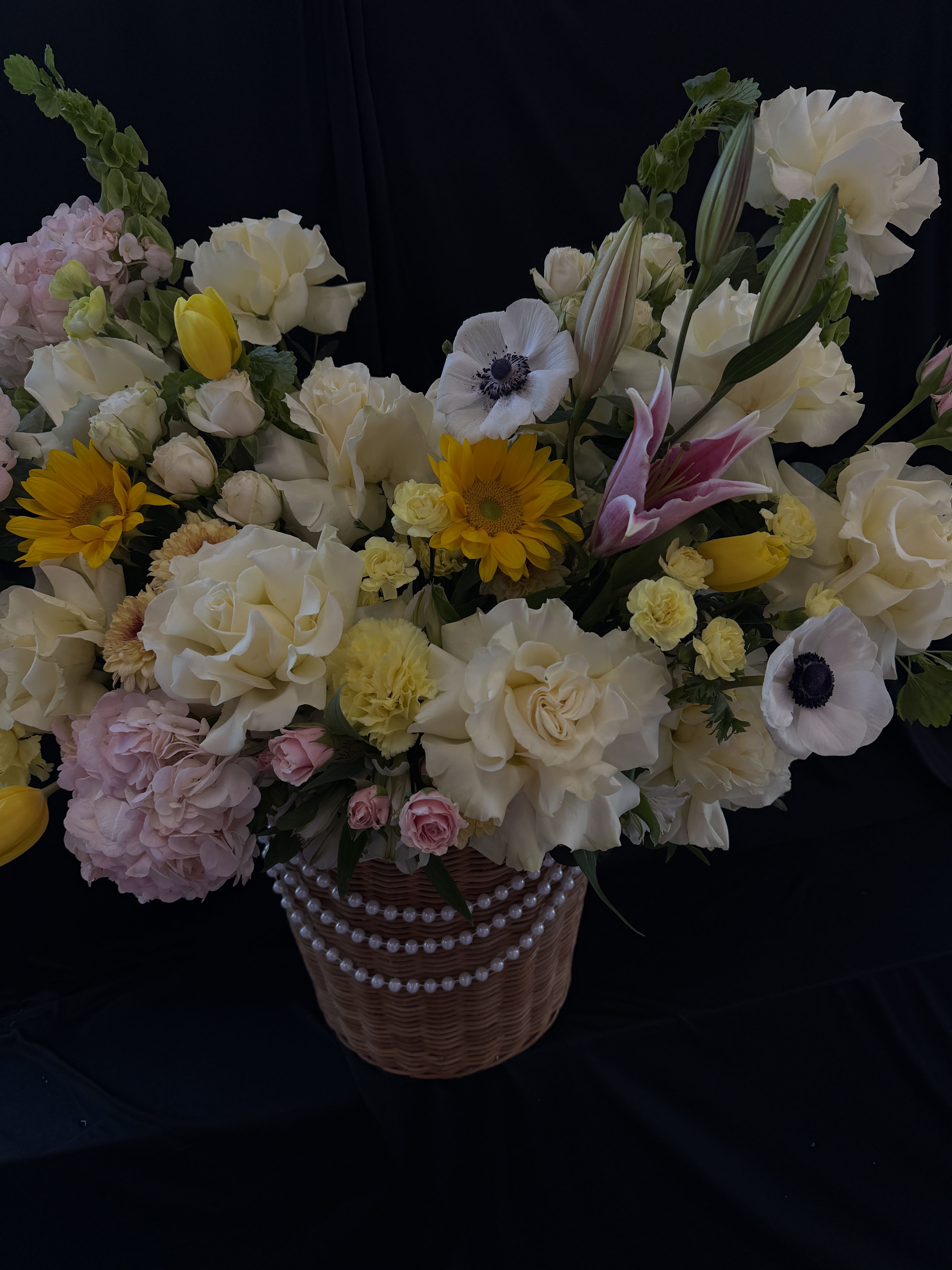 Soft Sunshine Garden -   “A graceful garden-style arrangement featuring cream roses, soft pink hydrangeas, sunflowers, stargazer lilies, and delicate anemones, beautifully accented with tulips, lisianthus, spray roses, carnations, and seasonal blooms, all styled with lush greenery in a charming pearl-detailed basket.”  If you want, I can make it more romantic, luxury, or shorter for Instagram 