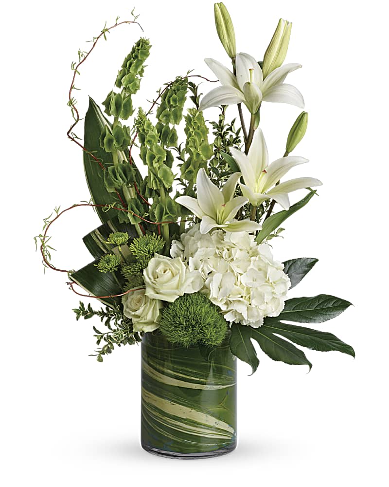 Tall arrangement of white lilies, roses, and hydrangeas with green accents in a clear glass cylinder vase