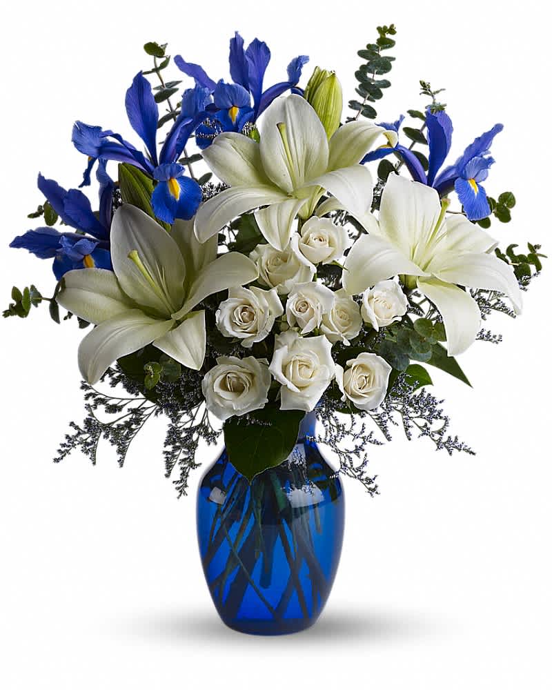 Arrangement of white lilies and roses with blue irises in a cobalt blue glass vase