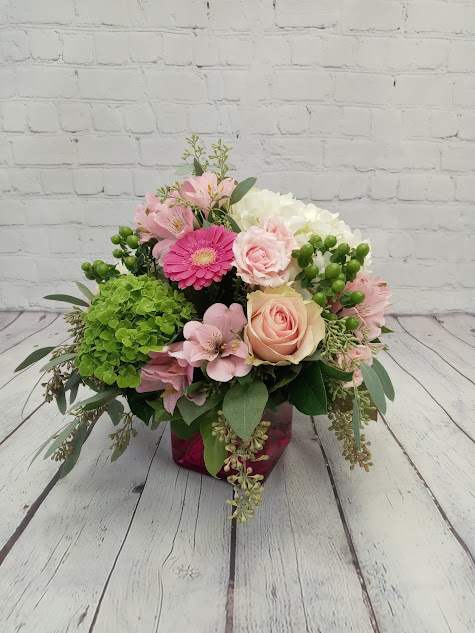 Low arrangement of pink roses and gerbera daisy with green hydrangeas in a pink glass cube vase