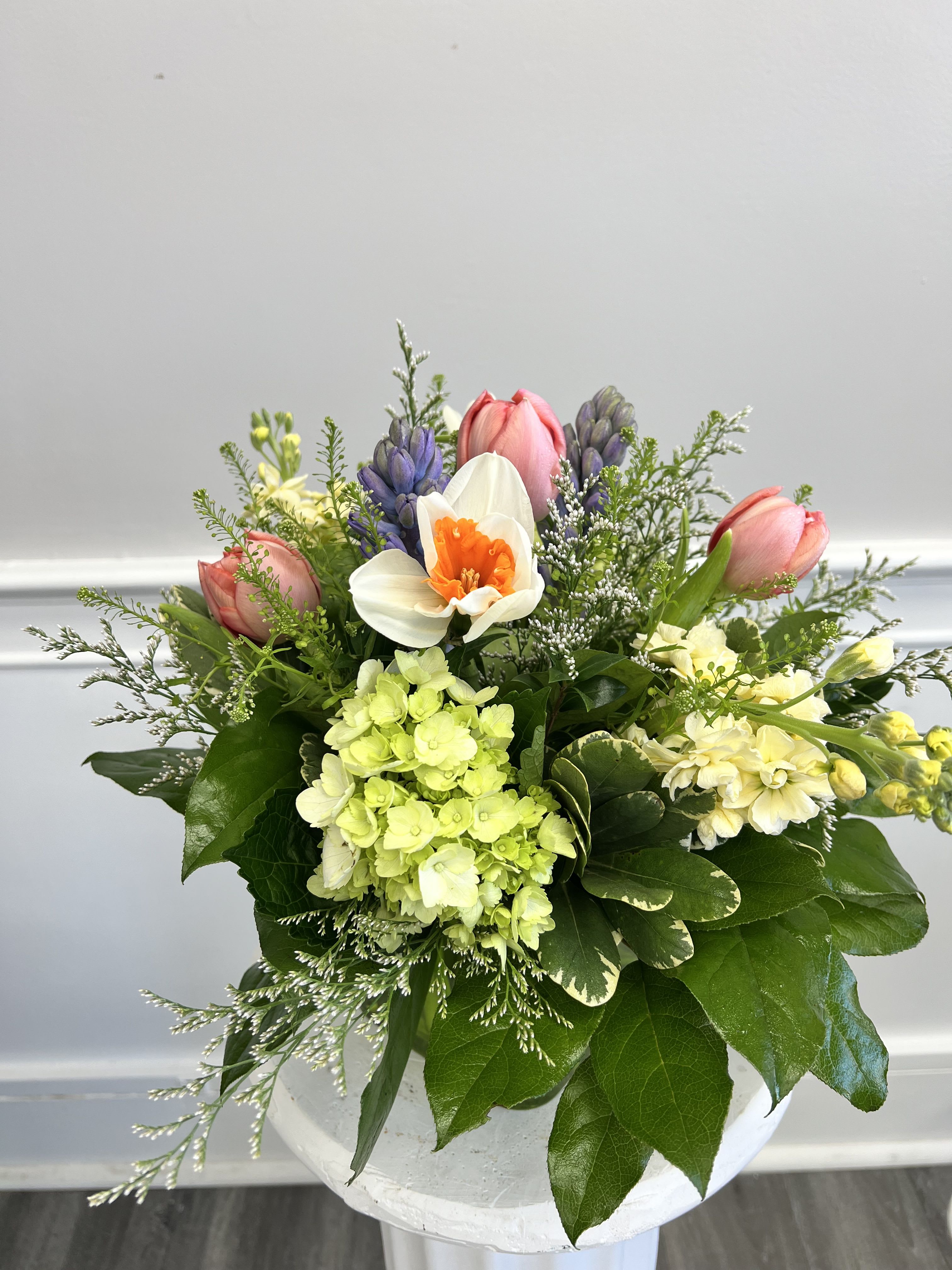 Spring bouquet with pink tulips, white daffodil, green hydrangea, and purple hyacinths in a white container