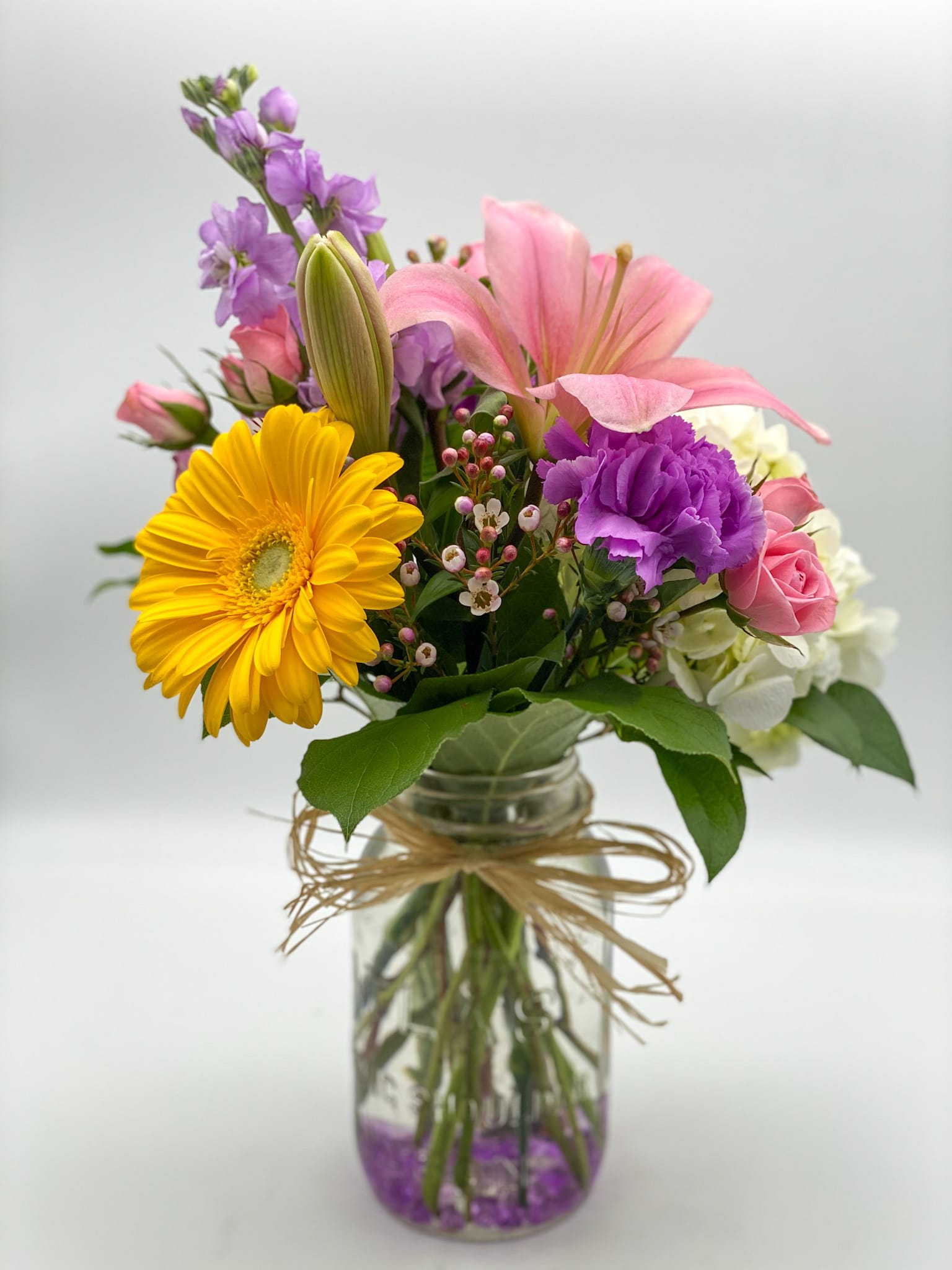 Mixed bouquet in a glass jar vase with pink, purple, yellow, and white blooms