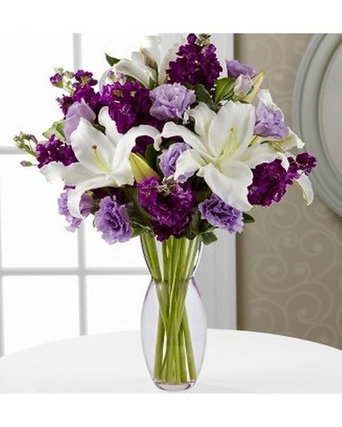 Timeless - This new Mother's Day classic starts with a gorgeous glass vase shimmering with a shade of subtle amethyst. From there, white lilies, lavender lisianthus, purple stock and green pittosporum make the polished purple palette their personal playground. 