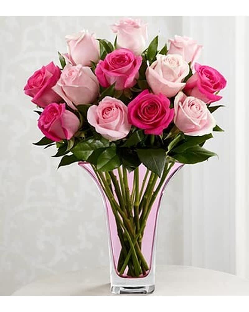 Arrangement of light and dark pink roses in a tall clear vase with pink accents