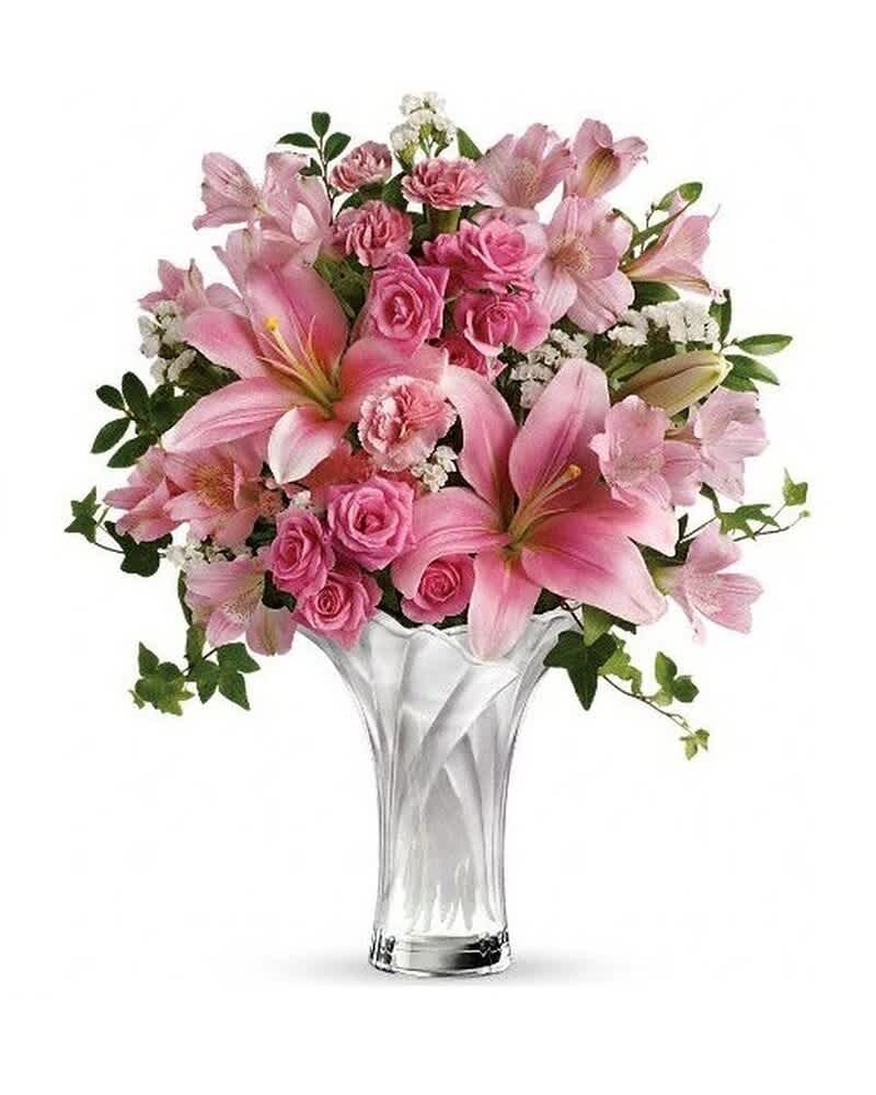 Pink lilies, roses, and carnations arranged in a fluted clear glass vase