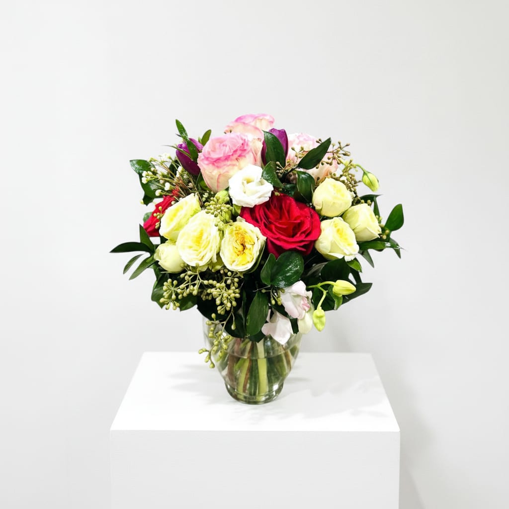 Bright My Day Bouquet  - A rounded cluster of roses and lisianthus in a clear glass vase delivers a bright, cheerful statement-perfect as a birthday bouquet or a just-because pick-me-up. The mix of orange, pink, red, yellow and white creates an uplifting color story that reads both romantic and celebratory, so she'll feel genuinely noticed whether you're saying happy birthday, thank you, or wishing a speedy recovery.  Densely gathered roses in buttery yellow, soft pink and vivid red blend into small white lisianthus accents for a lush, full look. Glossy dark foliage and small berries add textural contrast against the soft petals, and the simple clear glass vase keeps the focus on the flowers while fitting neatly on a table, desk, or bedside. Sized to make an immediate impression without overwhelming a space, this arrangement is an ideal summer centerpiece, a thoughtful Best Friends Day or Boss's Day gift, and an easy way to congratulate or celebrate someone special.