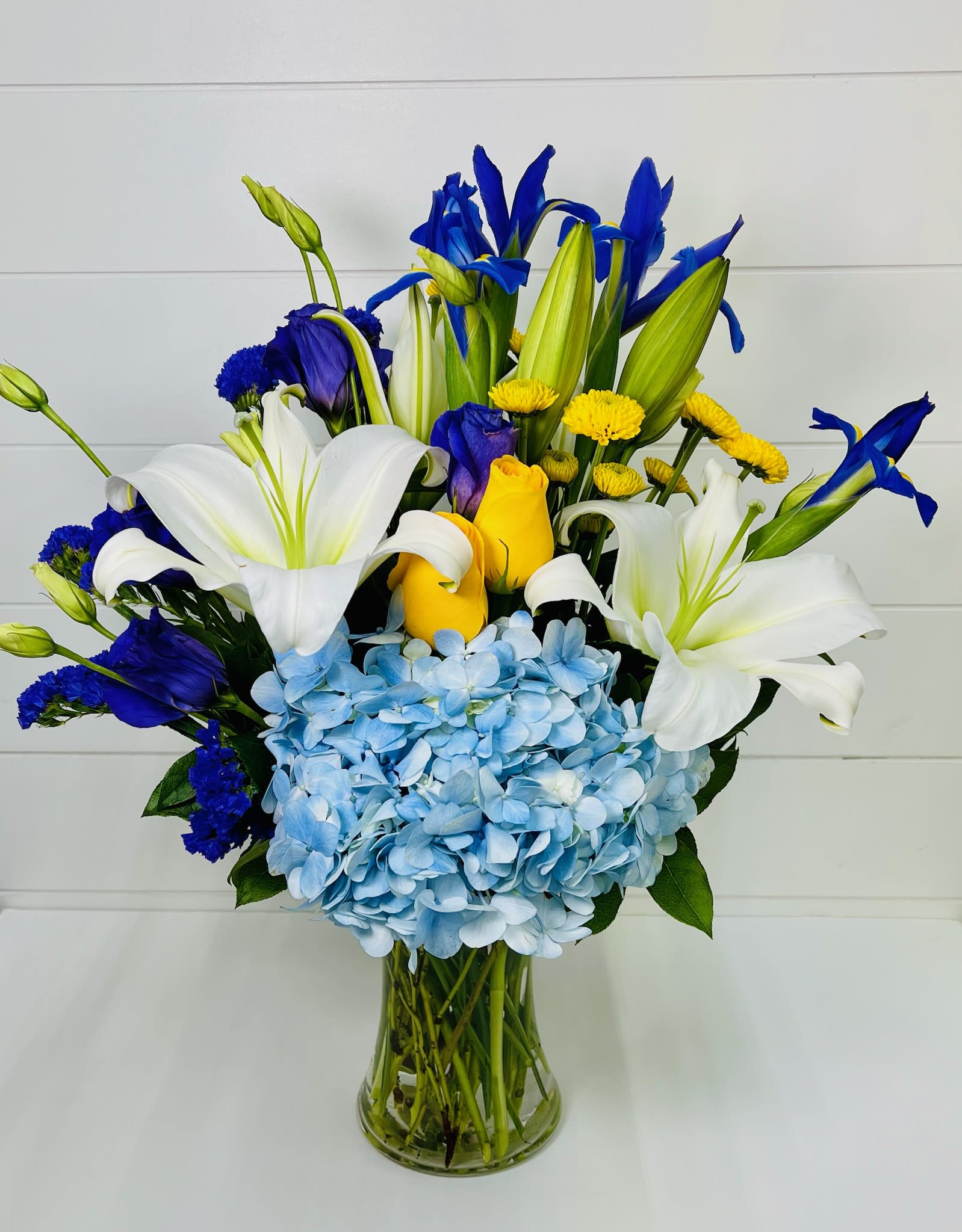 Spring Glow  - Spring Glow   Celebrate the beauty of spring with Spring Glow, a luxurious floral arrangement featuring hydrangeas, roses, tulips, lilies, and irises. This majestic mix of blue, yellow, and white blooms is artfully arranged in a classic glass vase, creating an elegant centerpiece perfect for birthdays, anniversaries, celebrations, or spring décor.  Available for flower delivery in Mableton, Smyrna, Austell, Marietta, and Atlanta, Spring Glow is handcrafted with premium seasonal flowers to bring vibrant spring beauty directly to any home or special occasion.  Order today to send a radiant, fresh spring bouquet that delights with color, elegance, and seasonal charm.