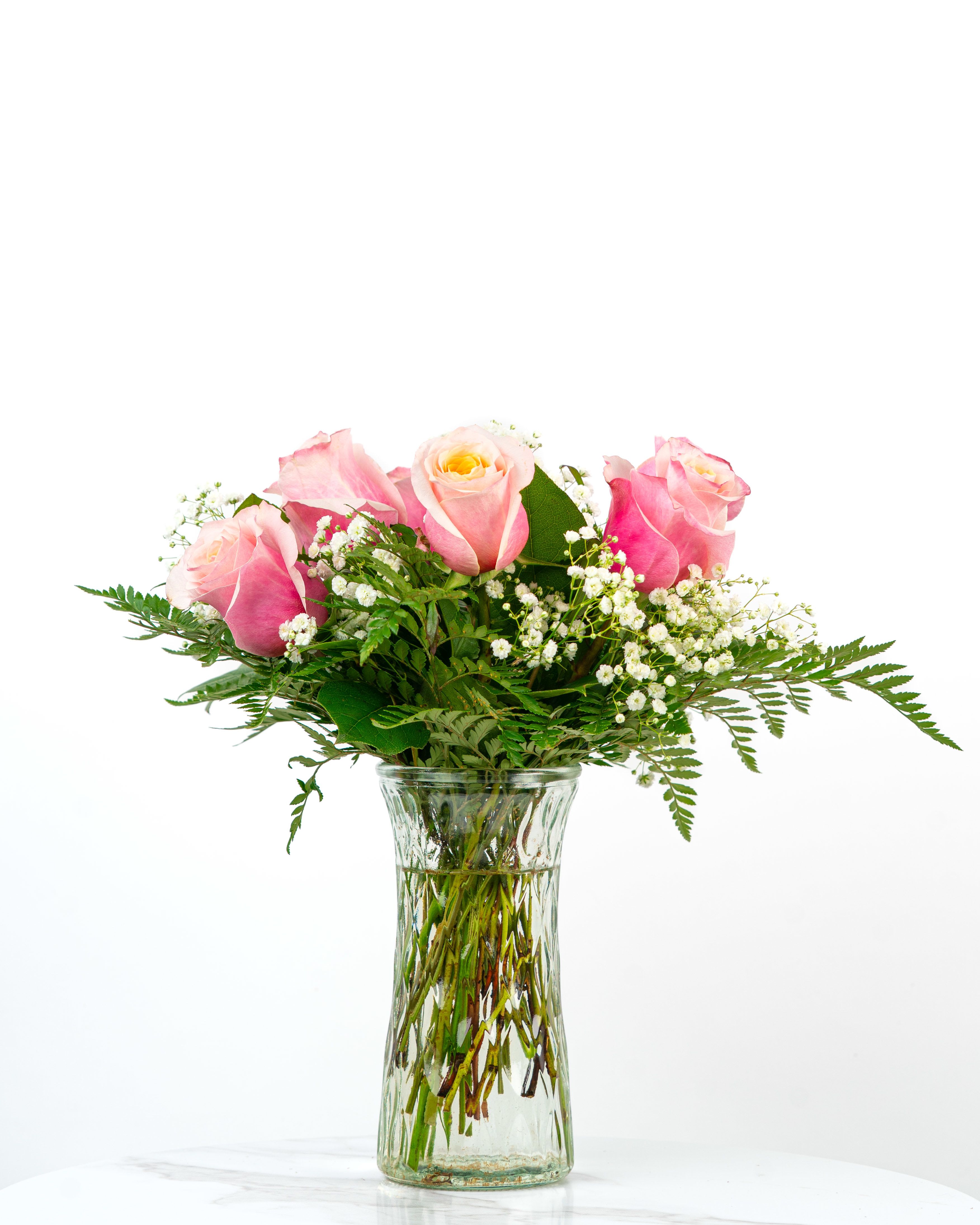 Pink roses with white filler flowers in a clear glass vase