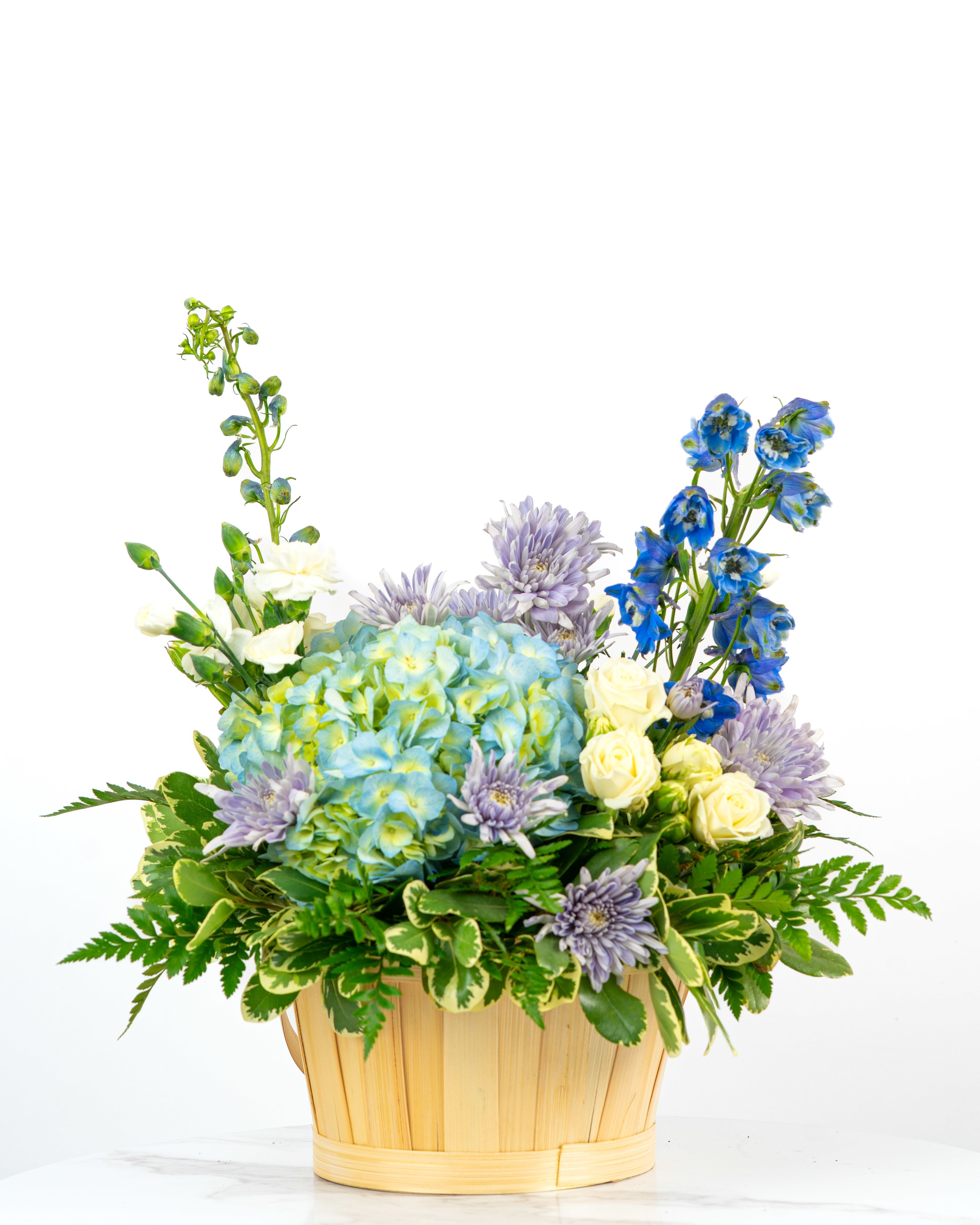 Basket arrangement with blue hydrangeas, white roses, lavender mums, and blue delphinium