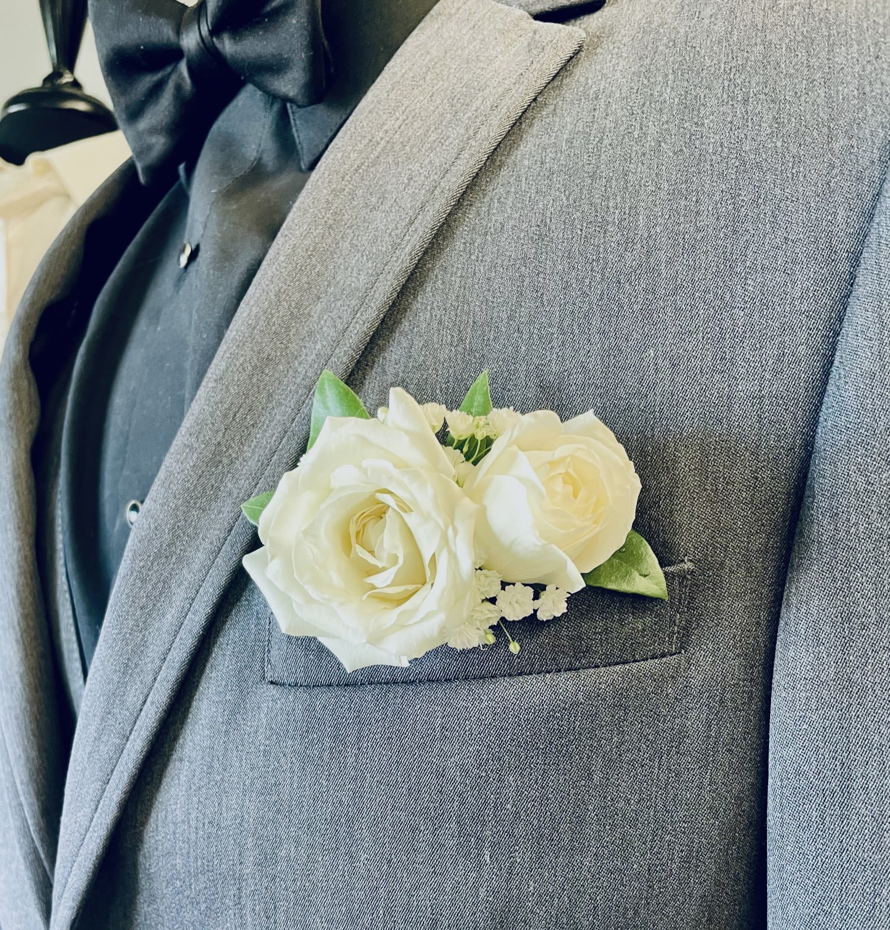 White rose pocket boutonniere on a gray suit jacket with black shirt and bow tie.