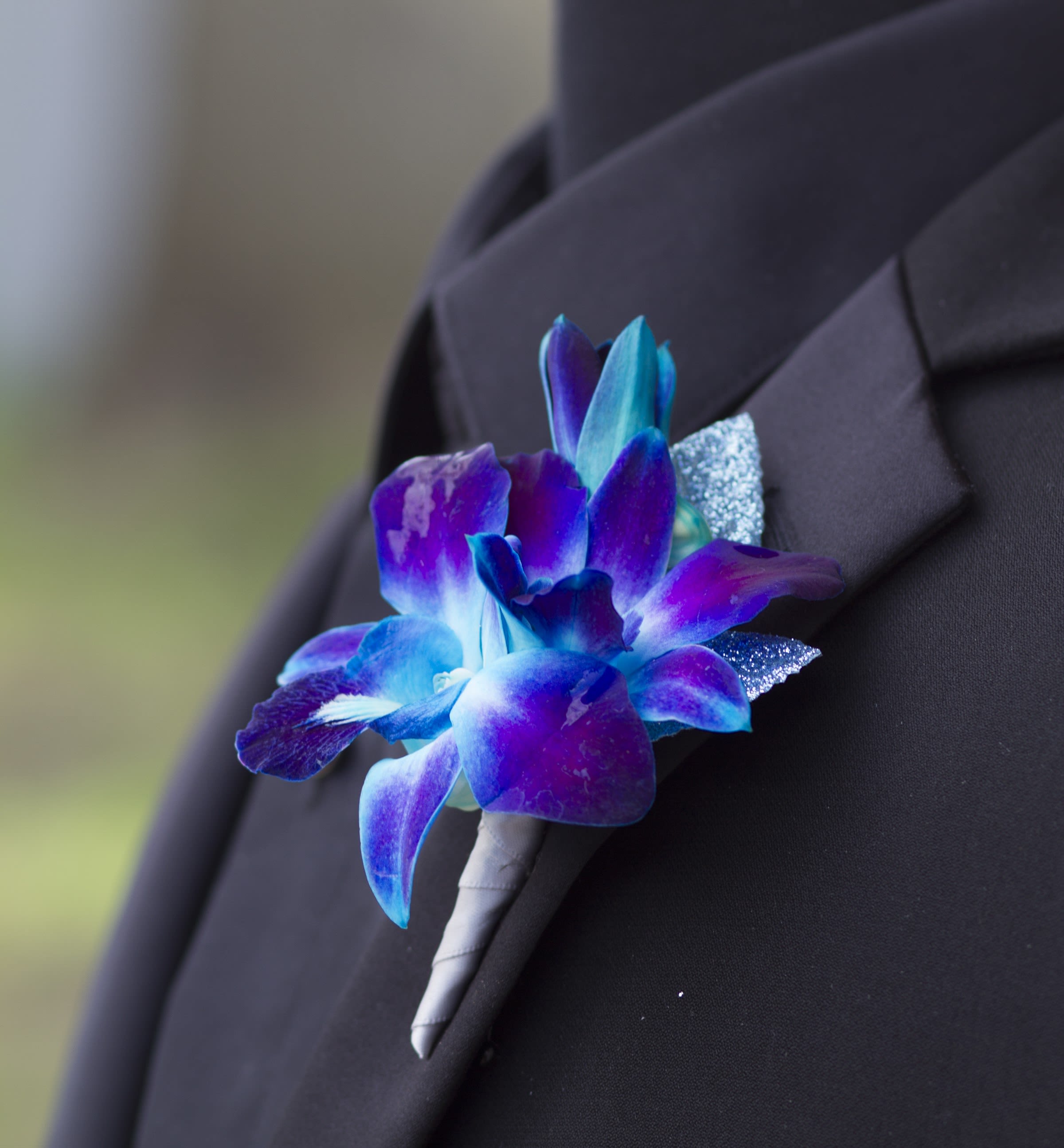 Blue and purple orchid boutonniere with glitter accents pinned to a black lapel