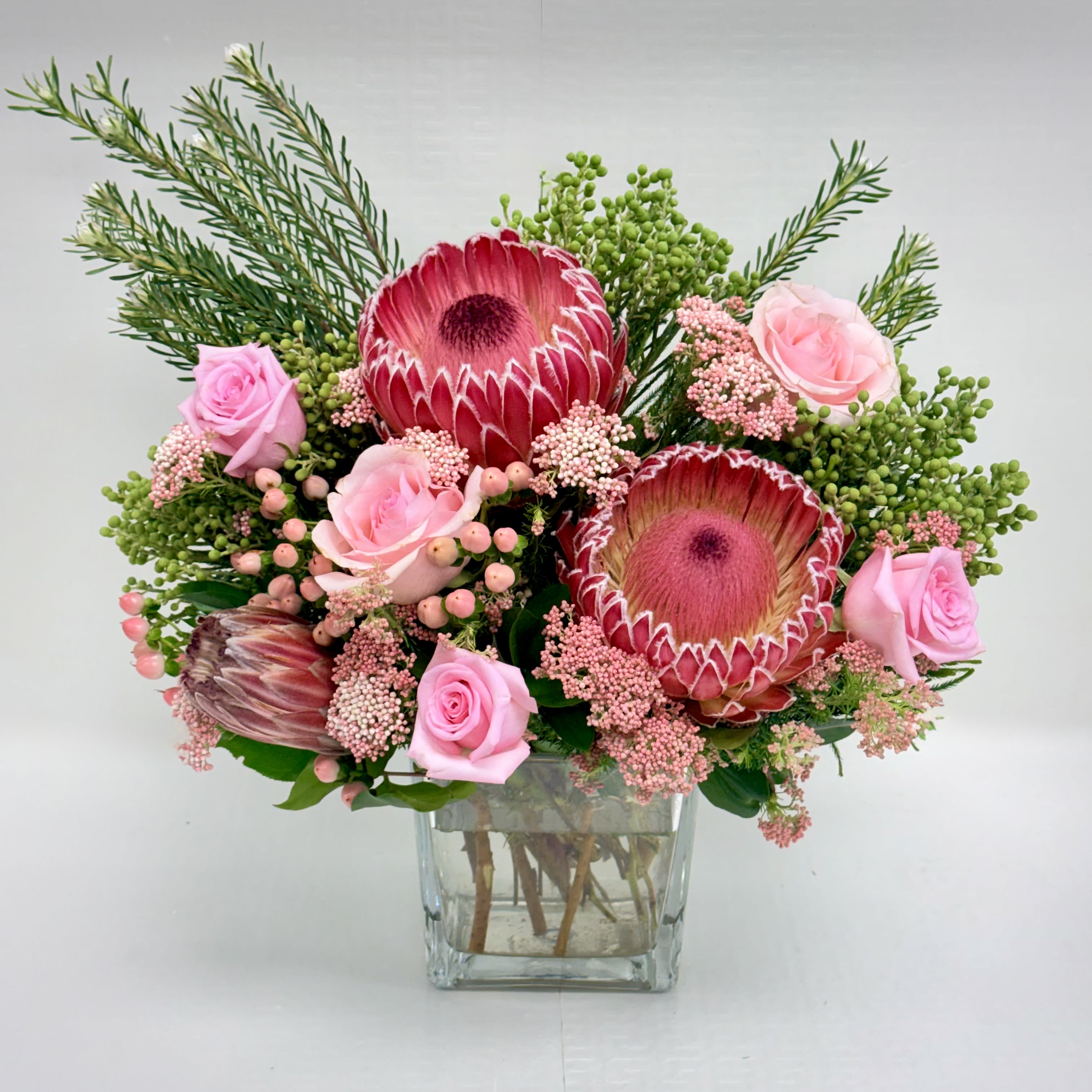 Bouquet of pink protea and roses with filler flowers in a clear glass cube vase