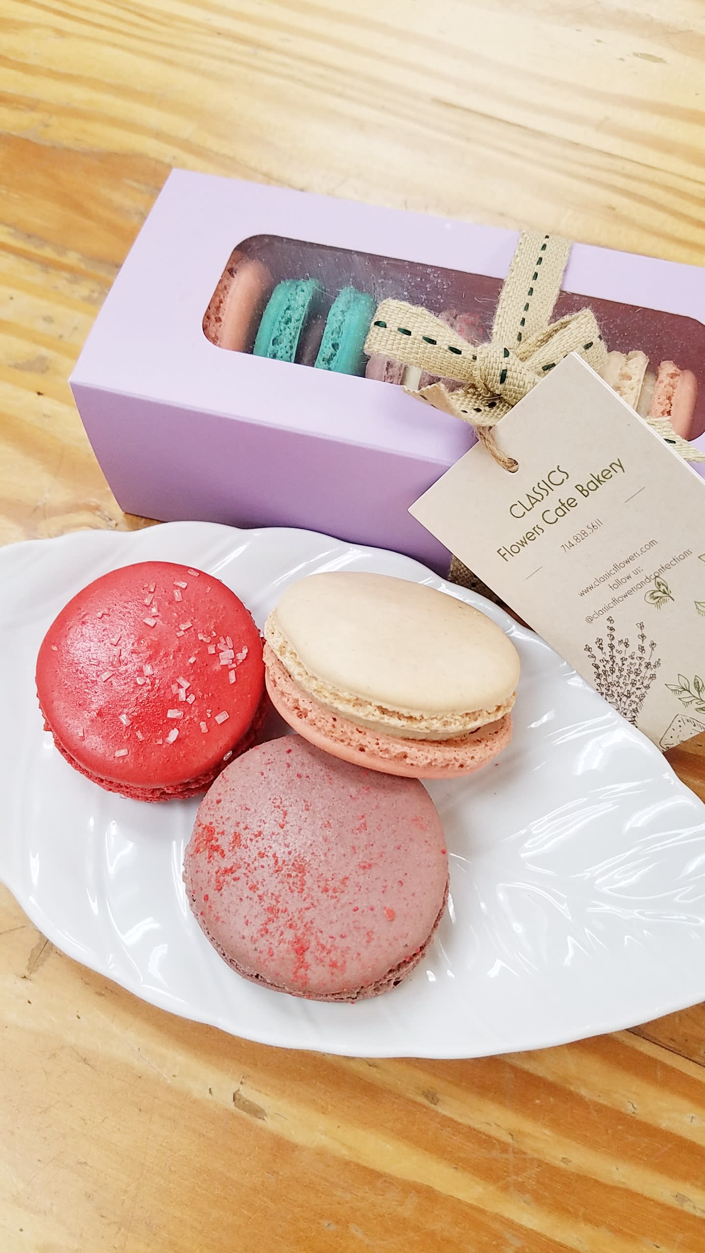 Assorted macarons on a white plate beside a lavender gift box with ribboned tag