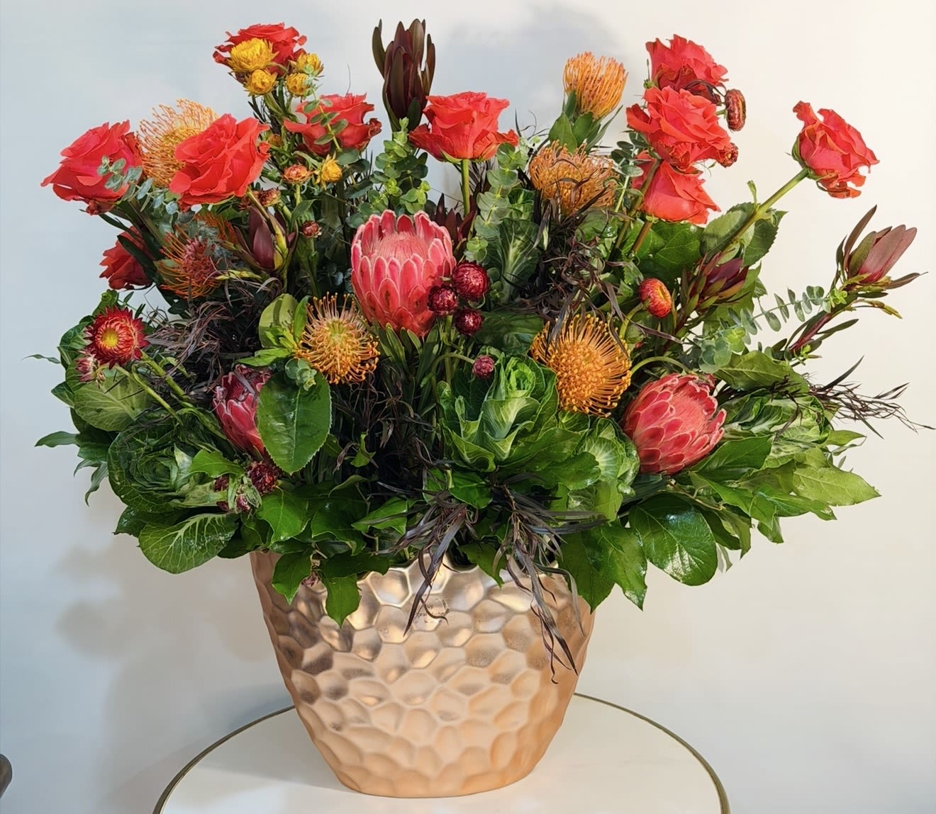 Wild Sunset Garden - A bold and vibrant floral arrangement designed to make a statement. This stunning piece combines rich red roses, exotic protea, textured pincushion blooms, and lush seasonal greenery in a modern ceramic vase. Perfect for celebrations, meaningful moments, or simply bringing warmth and color into any space. Handcrafted with care at Guy Floral Studio, each arrangement is uniquely designed with fresh, premium flowers to ensure long lasting beauty and impact. We proudly offer same day flower delivery for orders placed before cutoff time, making it easy to send something beautiful right when it matters most. Available for delivery in: Beverly Hills, Bel Air, West Hollywood, Beverly Grove, Studio City, Sherman Oaks, Encino, Hollywood, Hollywood Hills, Culver City, Santa Monica and surrounding areas.